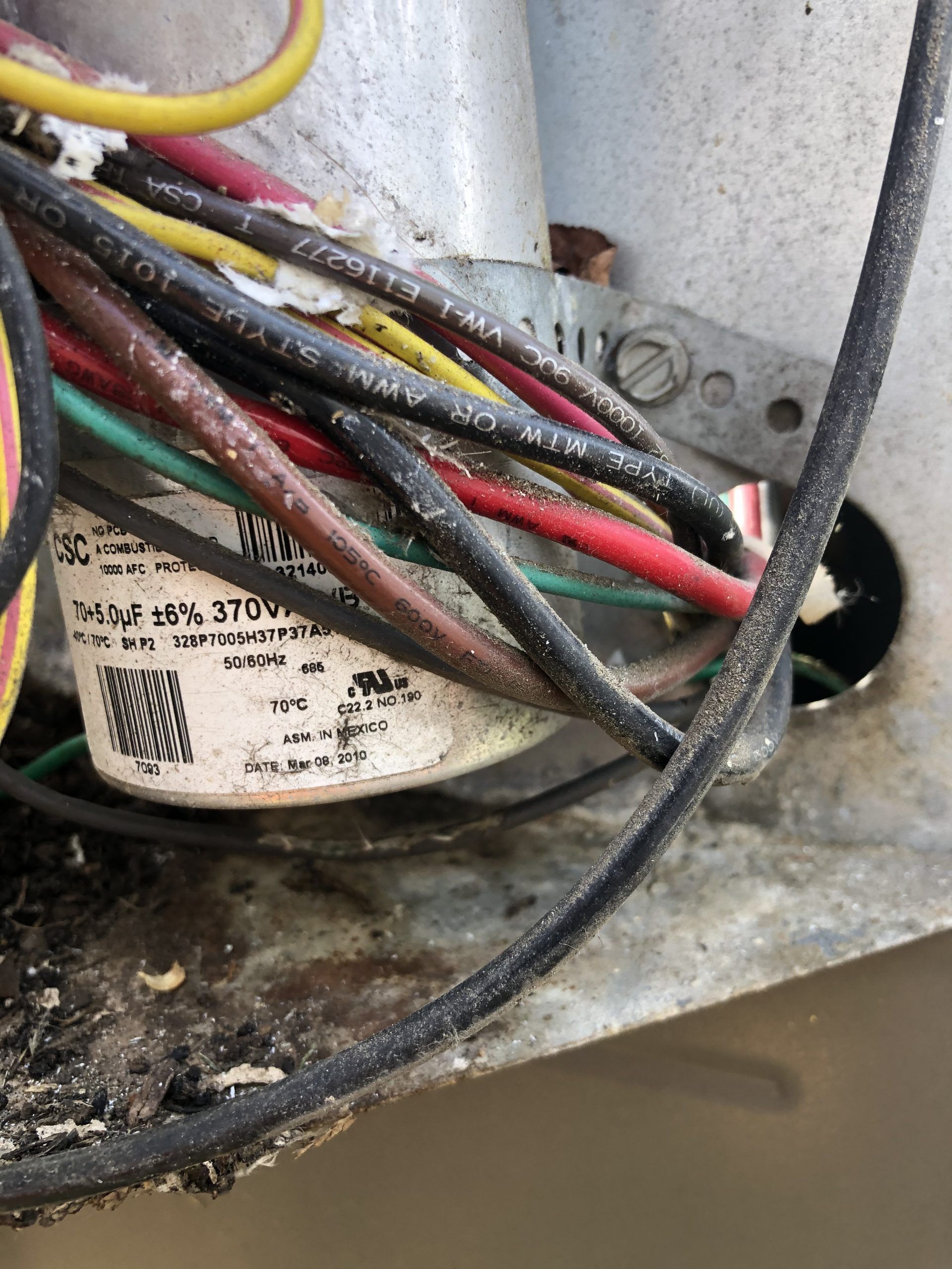 Damaged wires near an air conditioner capacitor, with black and red wires visible.