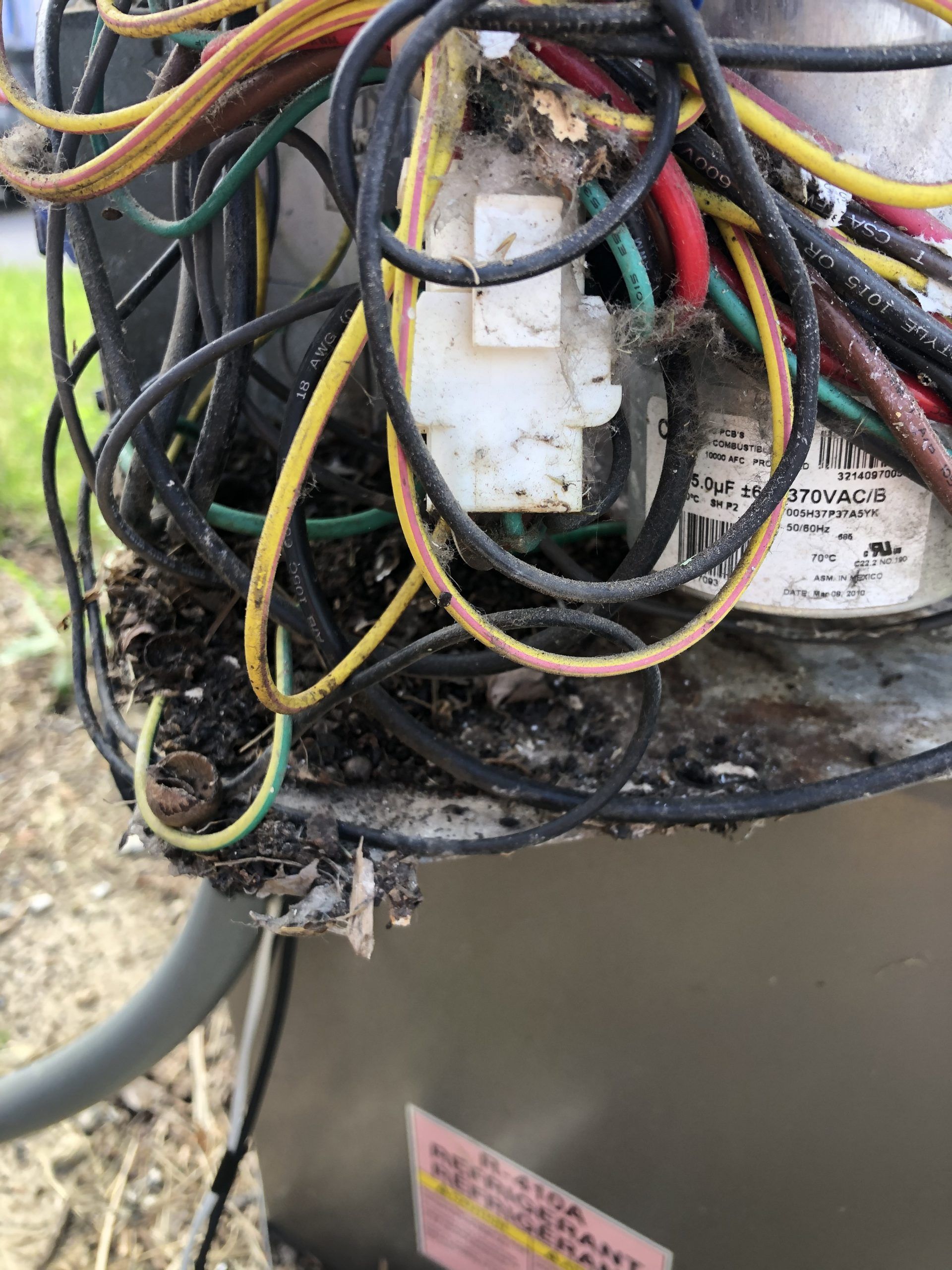 Close-up of an air conditioning unit's electrical components with exposed wires, covered in debris.