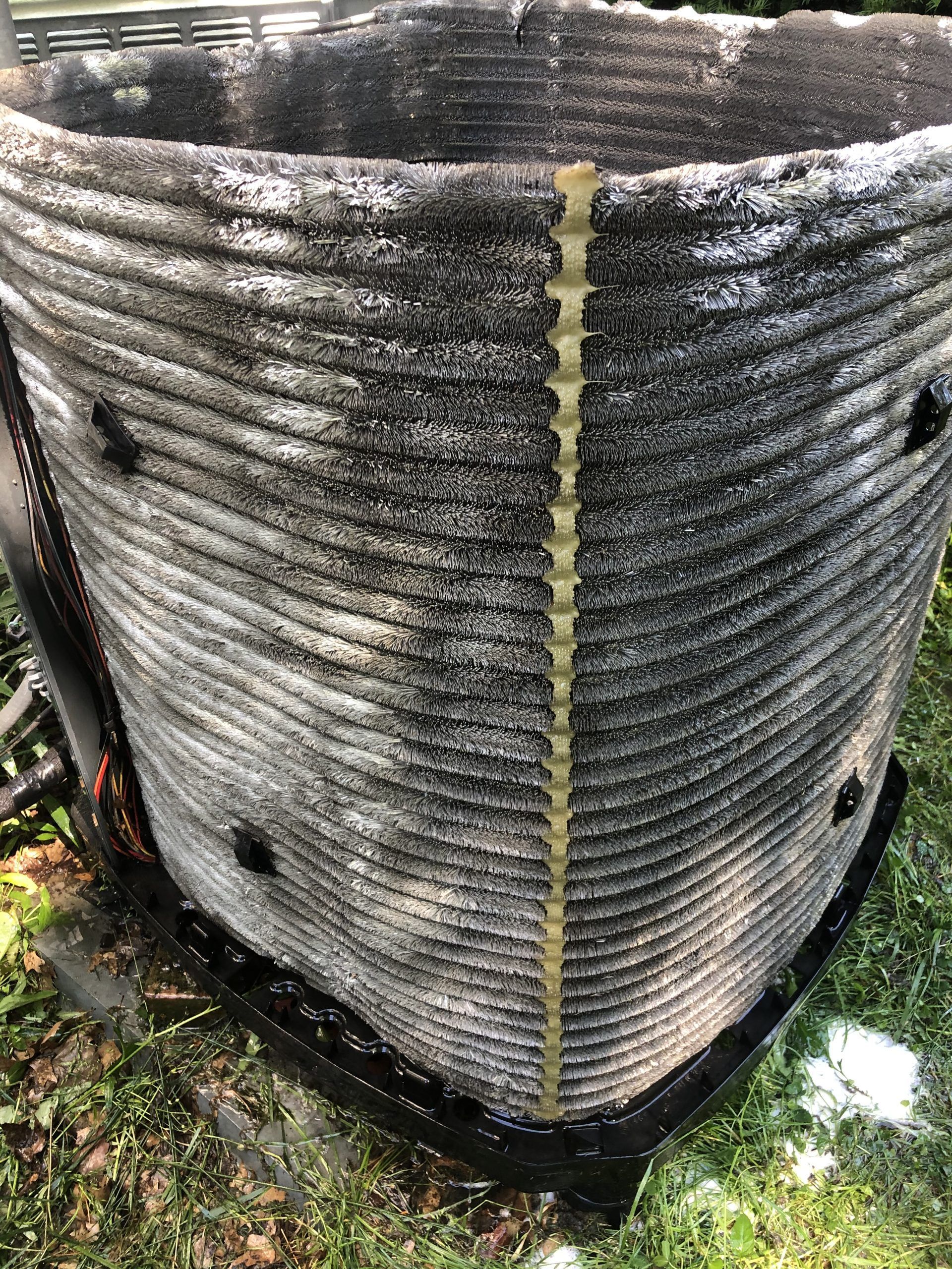 Black and gray outdoor air conditioning unit coil, showing horizontal lines, with yellow vertical support.