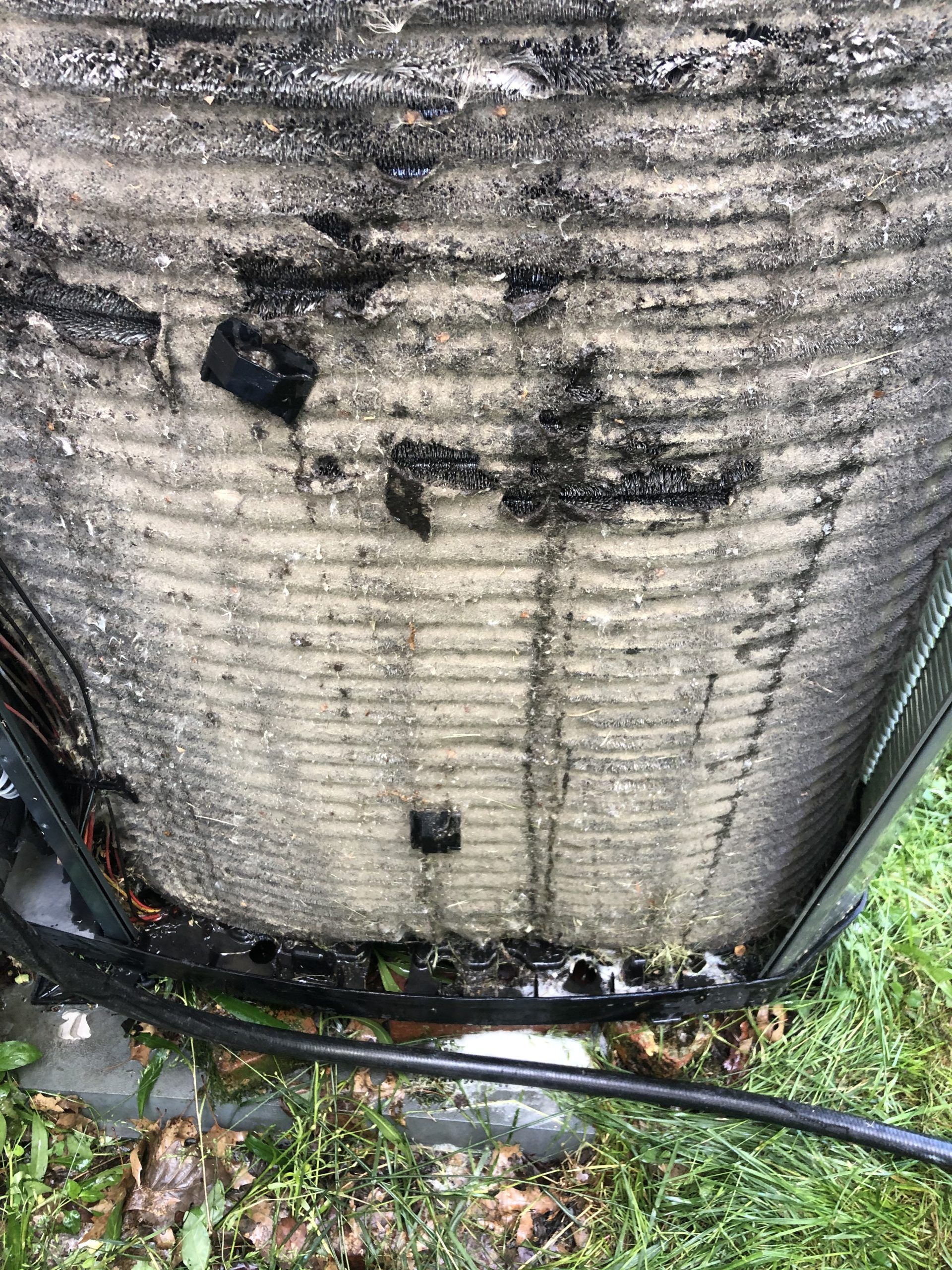 Close-up of a dirty, outdoor air conditioning unit coil, covered in dust and debris, with some black residue.