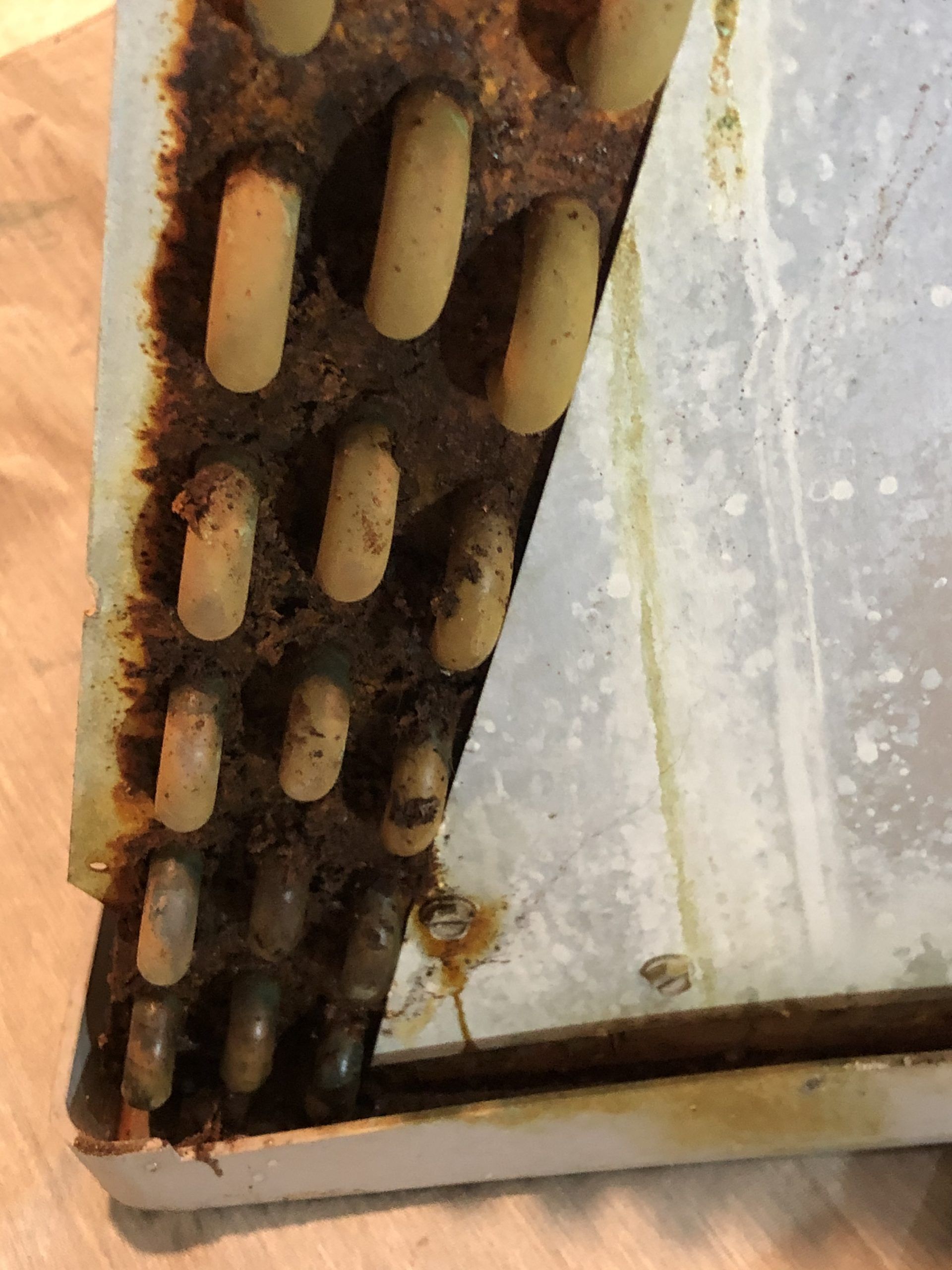 Close-up of a dirty, corroded air conditioning coil, coated with brown grime.