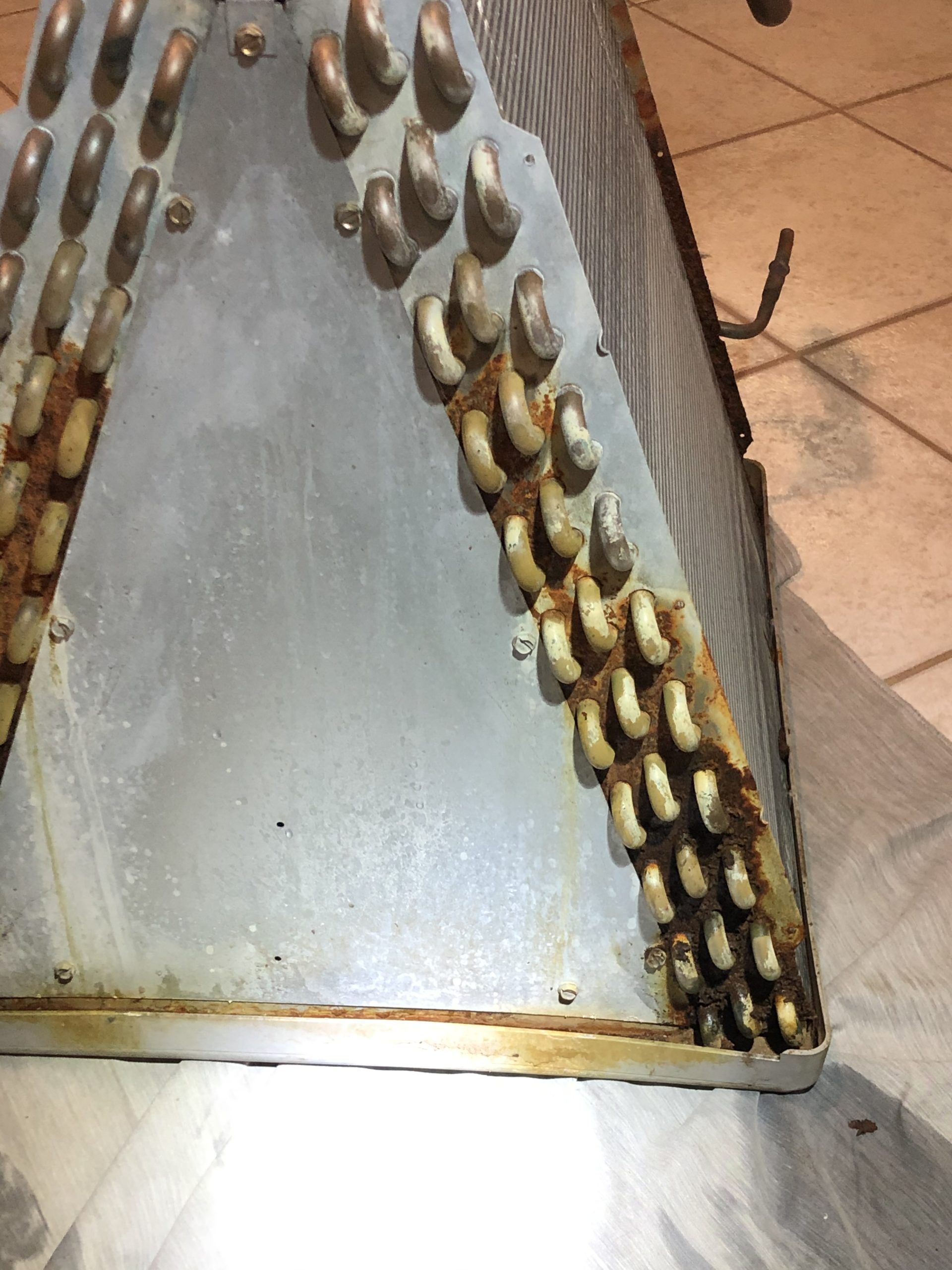 Corroded metal cooling coil with rust, angled design, in a room.