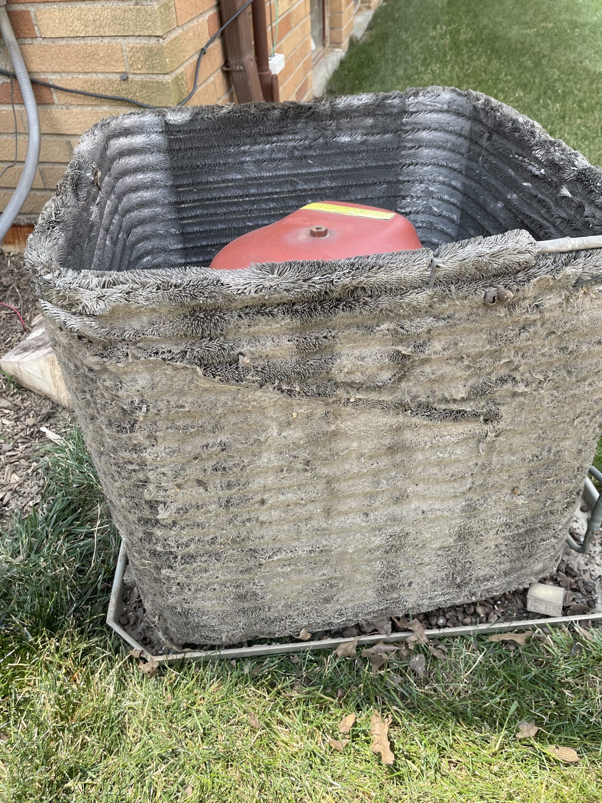 Outdoor air conditioning unit with a rusty-colored component inside and grimy exterior.
