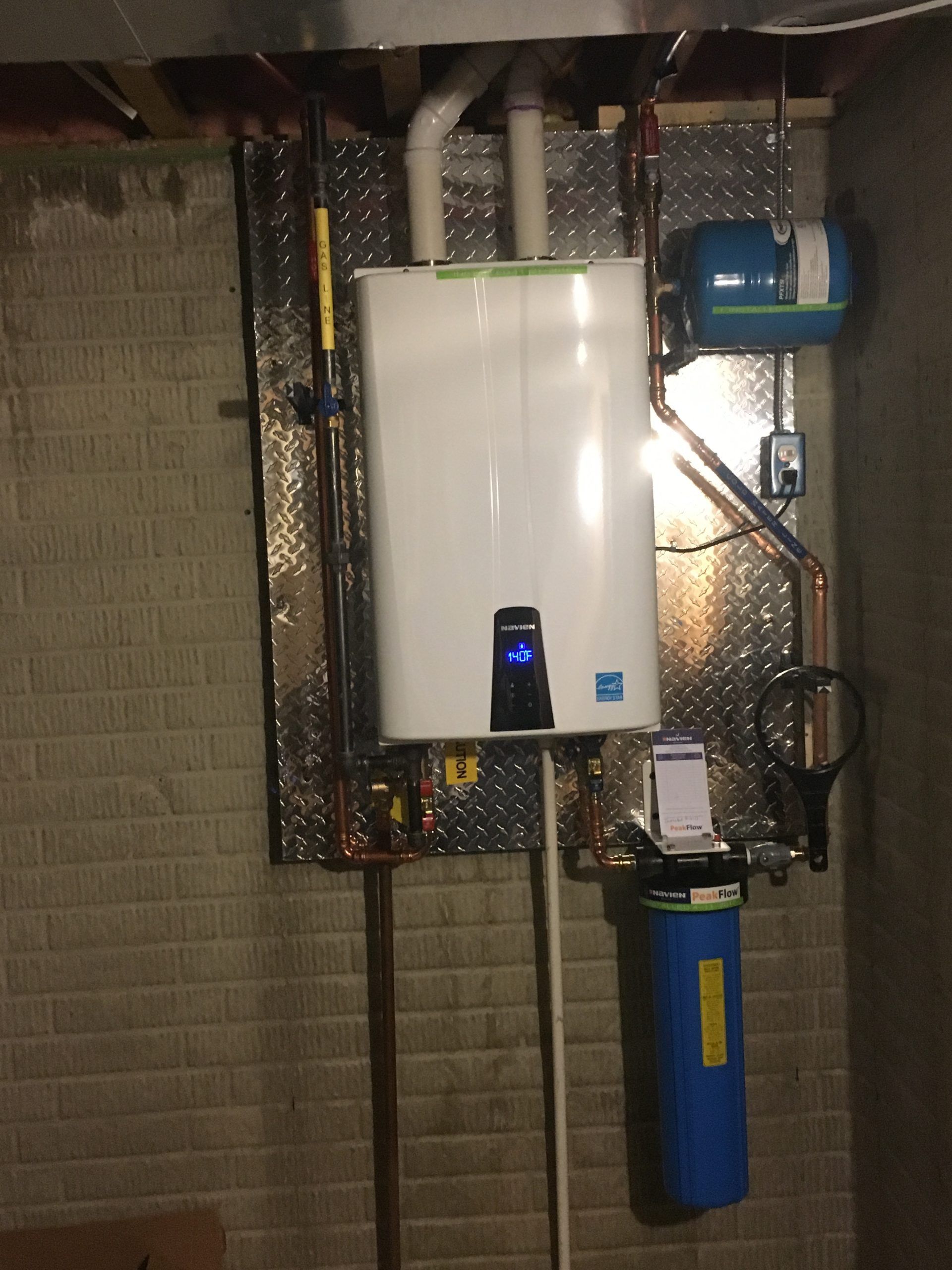 Tankless water heater and components mounted on a wall in a basement.