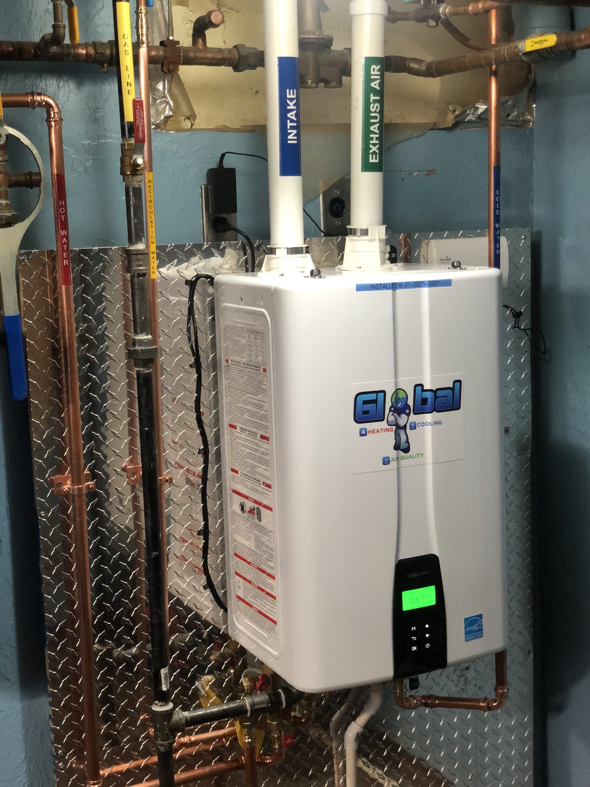 A white Global water heater installed on a diamond plate metal backboard in a basement.