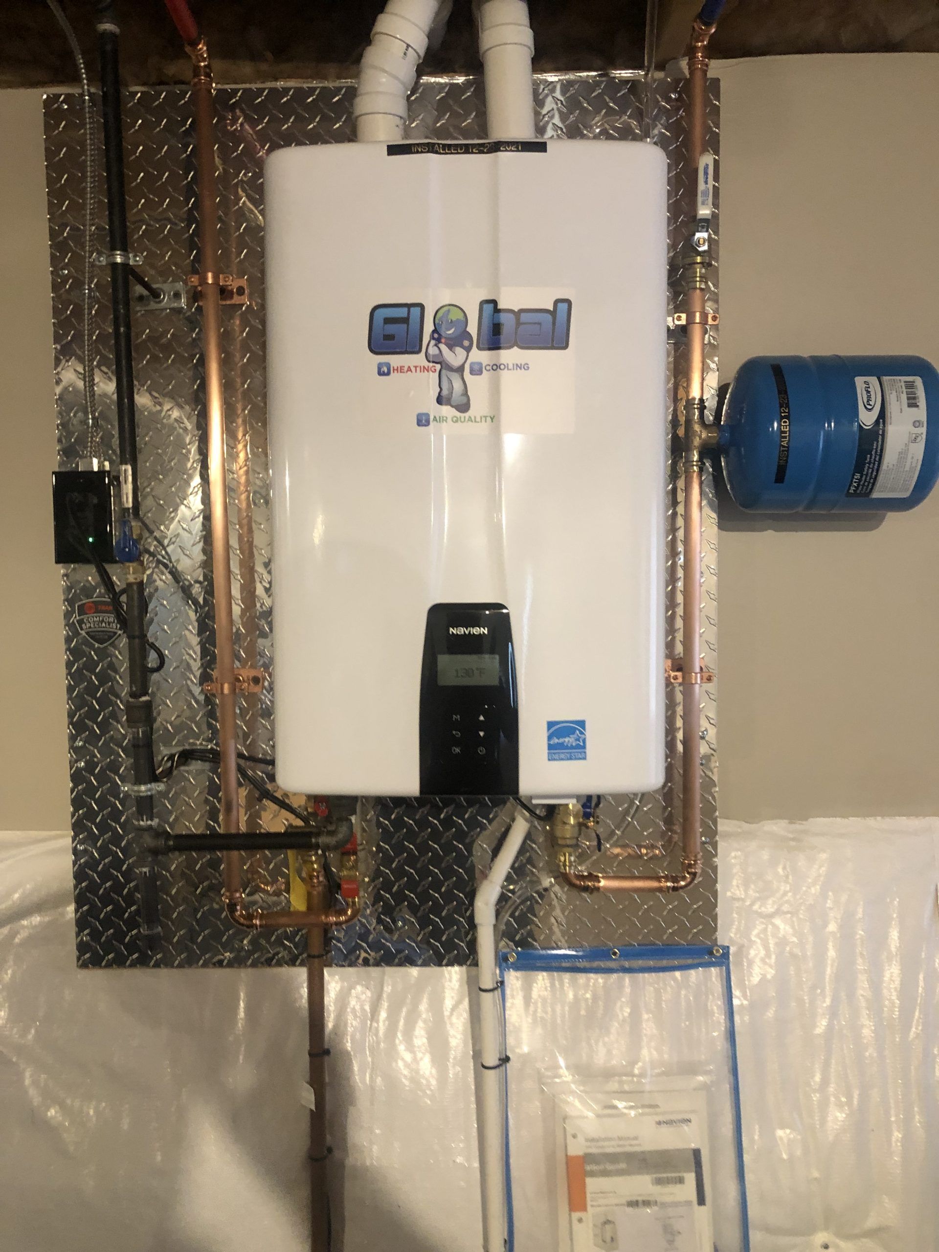A wall-mounted water heater with copper pipes and a blue expansion tank on a metallic diamond-plate background.