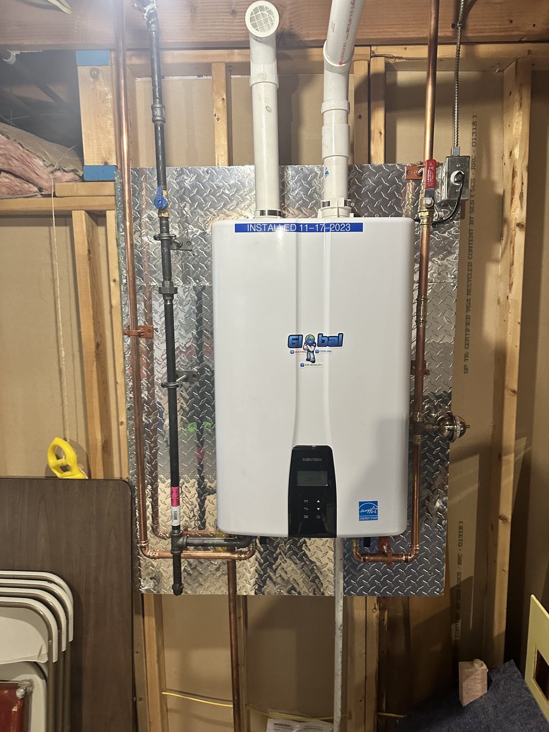 A white tankless water heater mounted on a wall with pipes and connections.