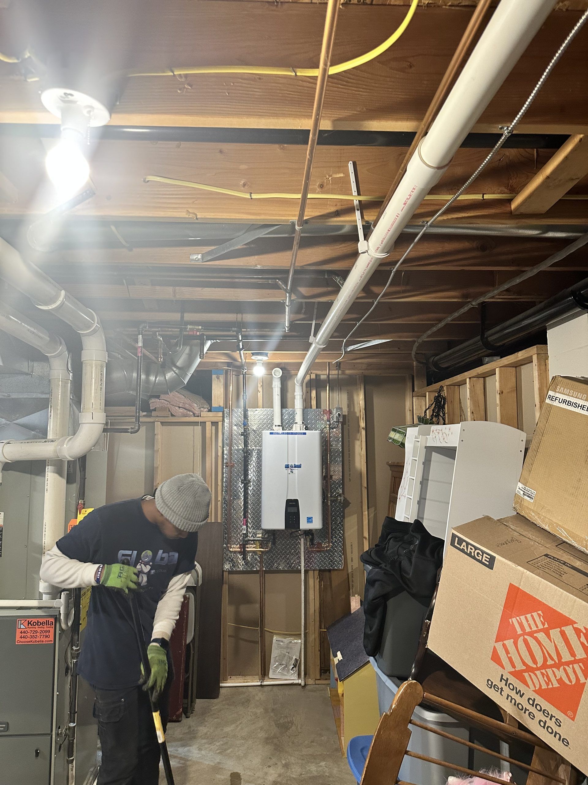 Man working on HVAC system in basement with piping and boxes.