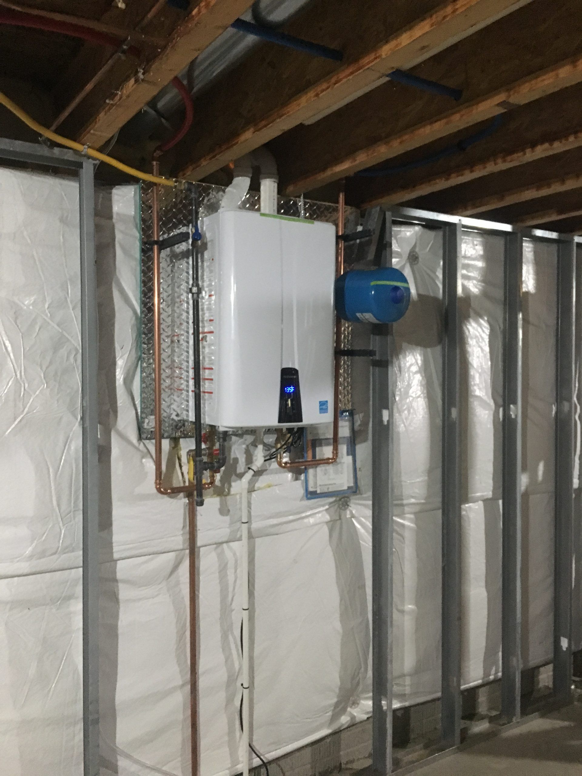 Tankless water heater mounted on a basement wall with associated pipes and equipment.