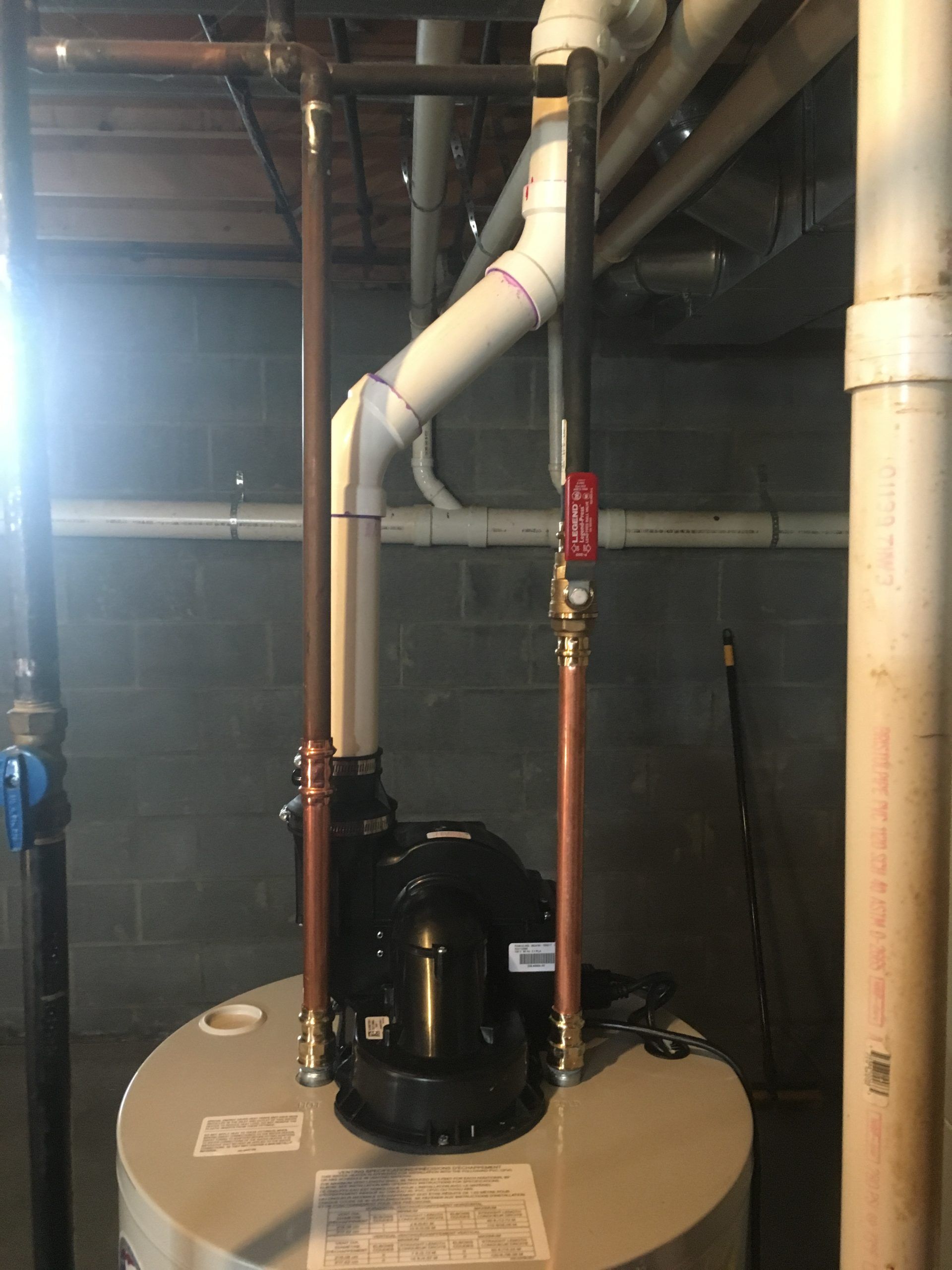 Water heater with copper pipes, white PVC, and black pump in a basement setting.
