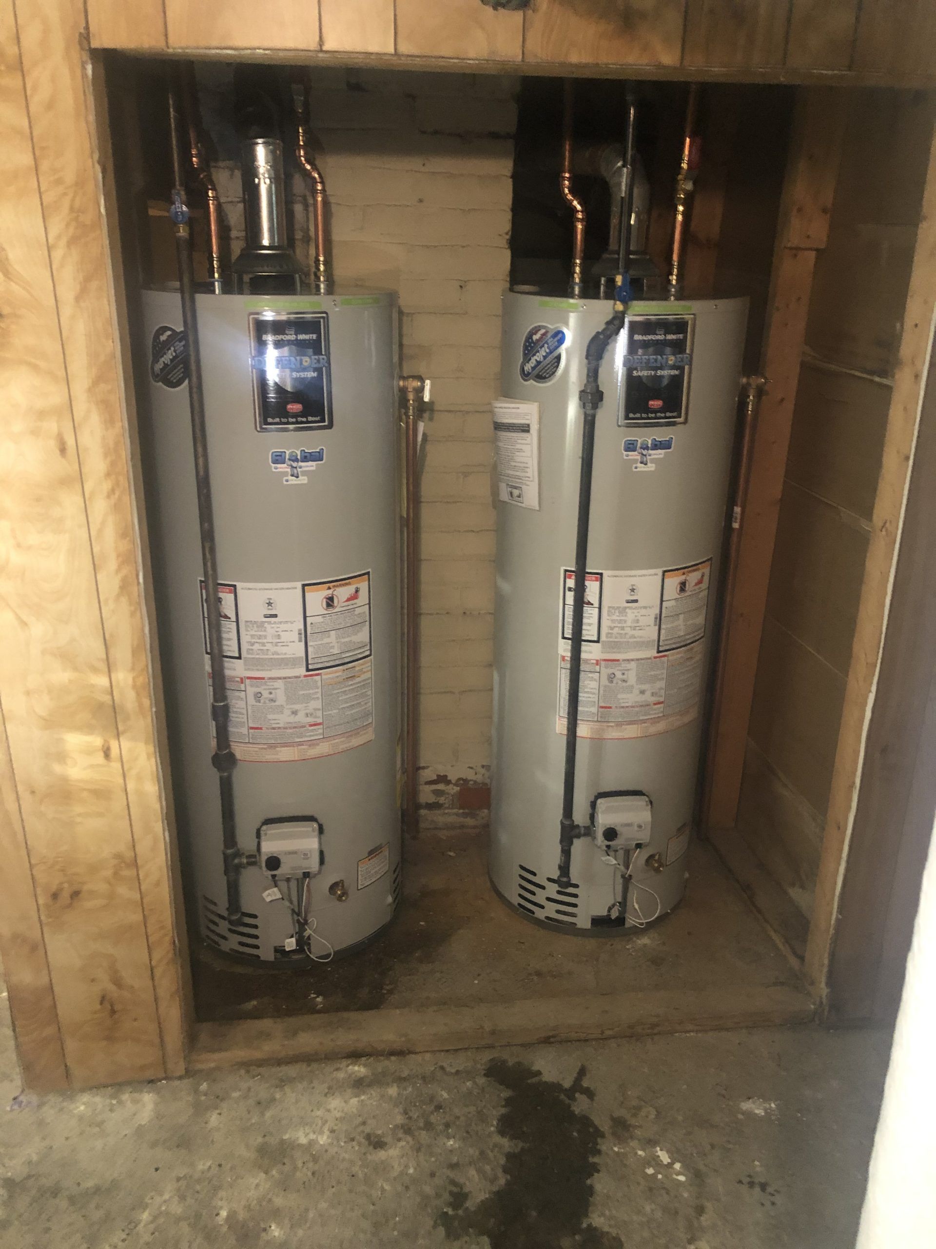 Two water heaters in a wooden alcove; gray tanks with copper pipes.