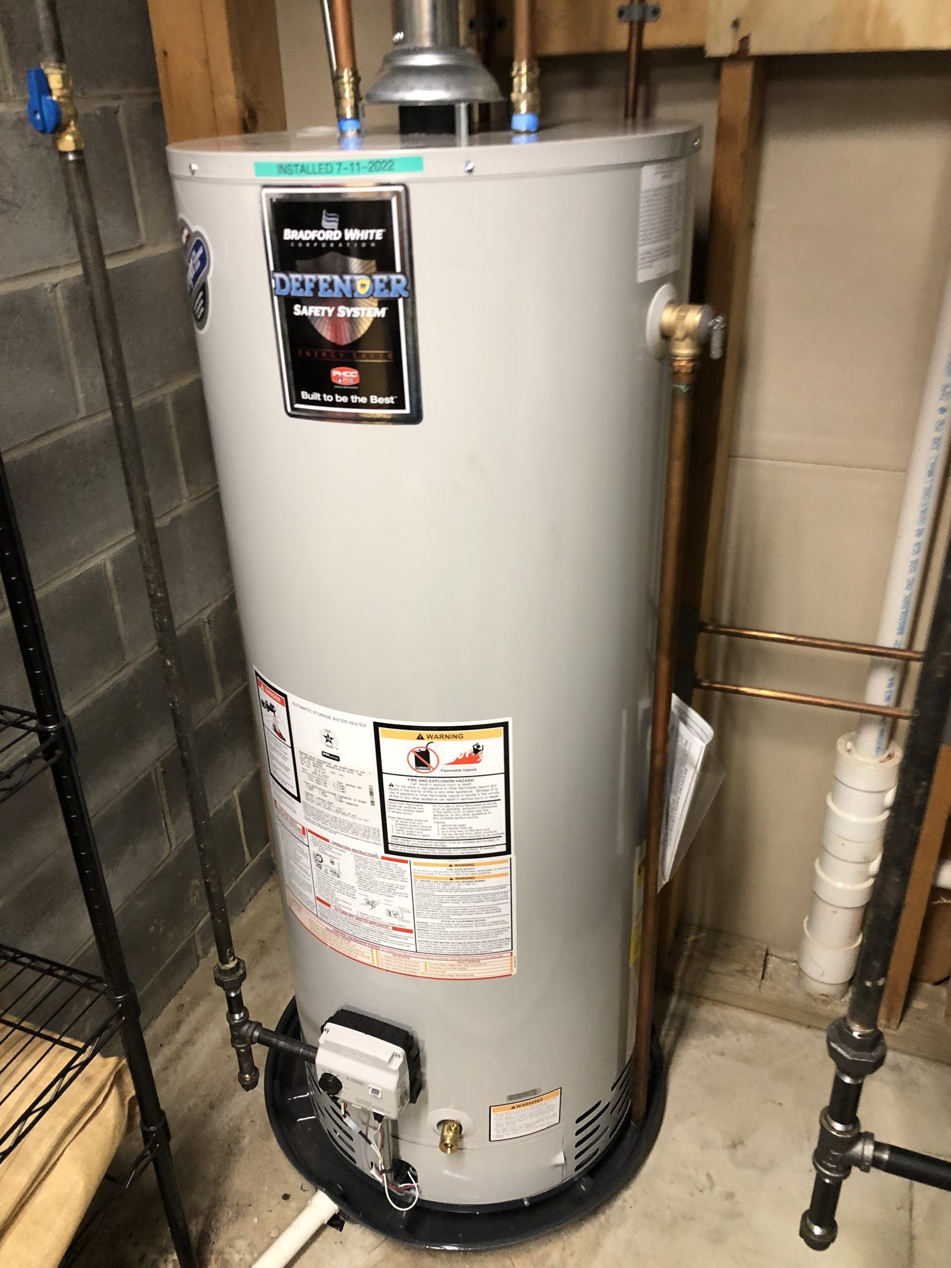 A tall, cylindrical hot water heater in a utility room; gray with copper pipes and a black base.