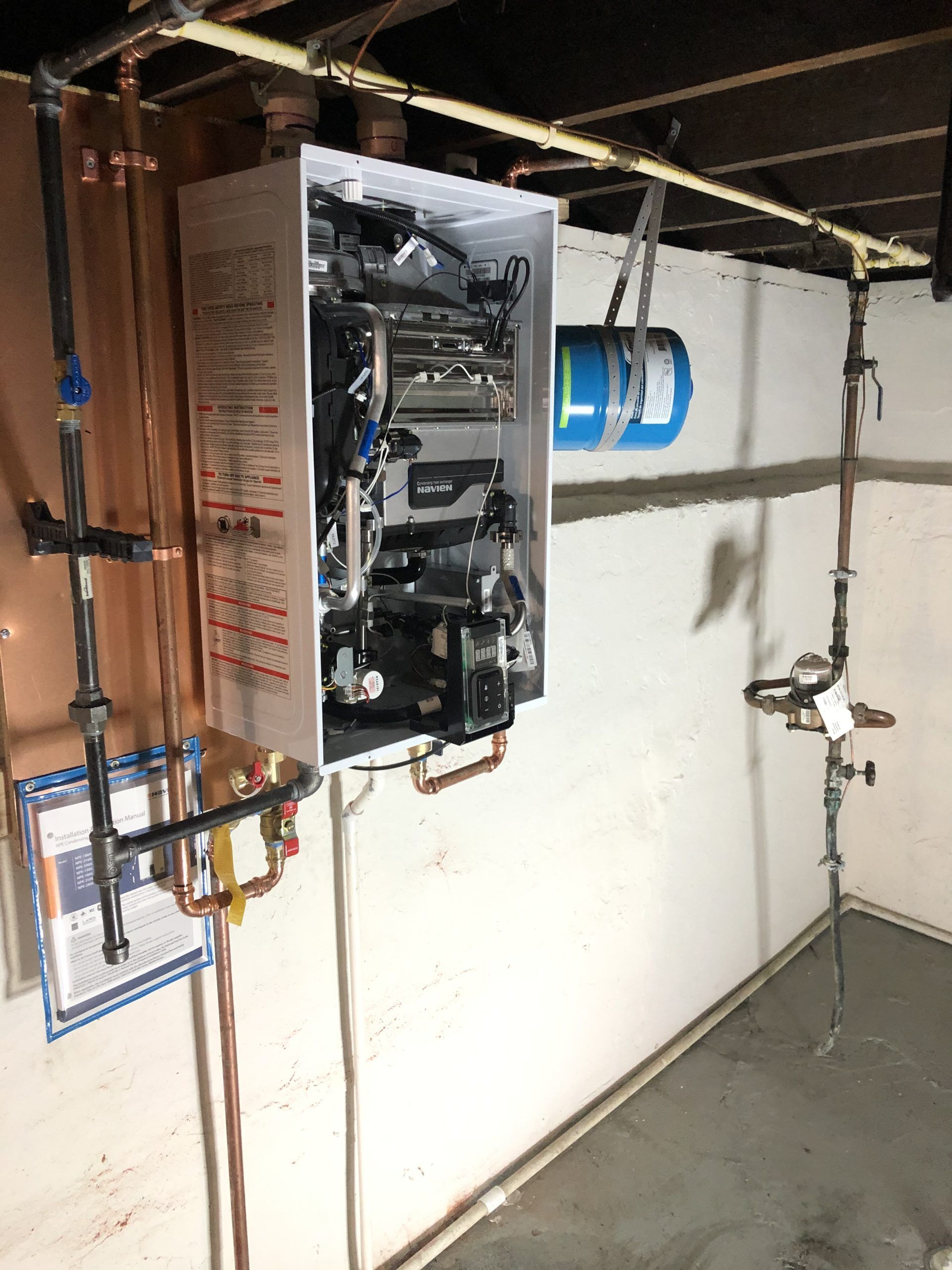 Tankless water heater installed on a basement wall with connected pipes and expansion tank.