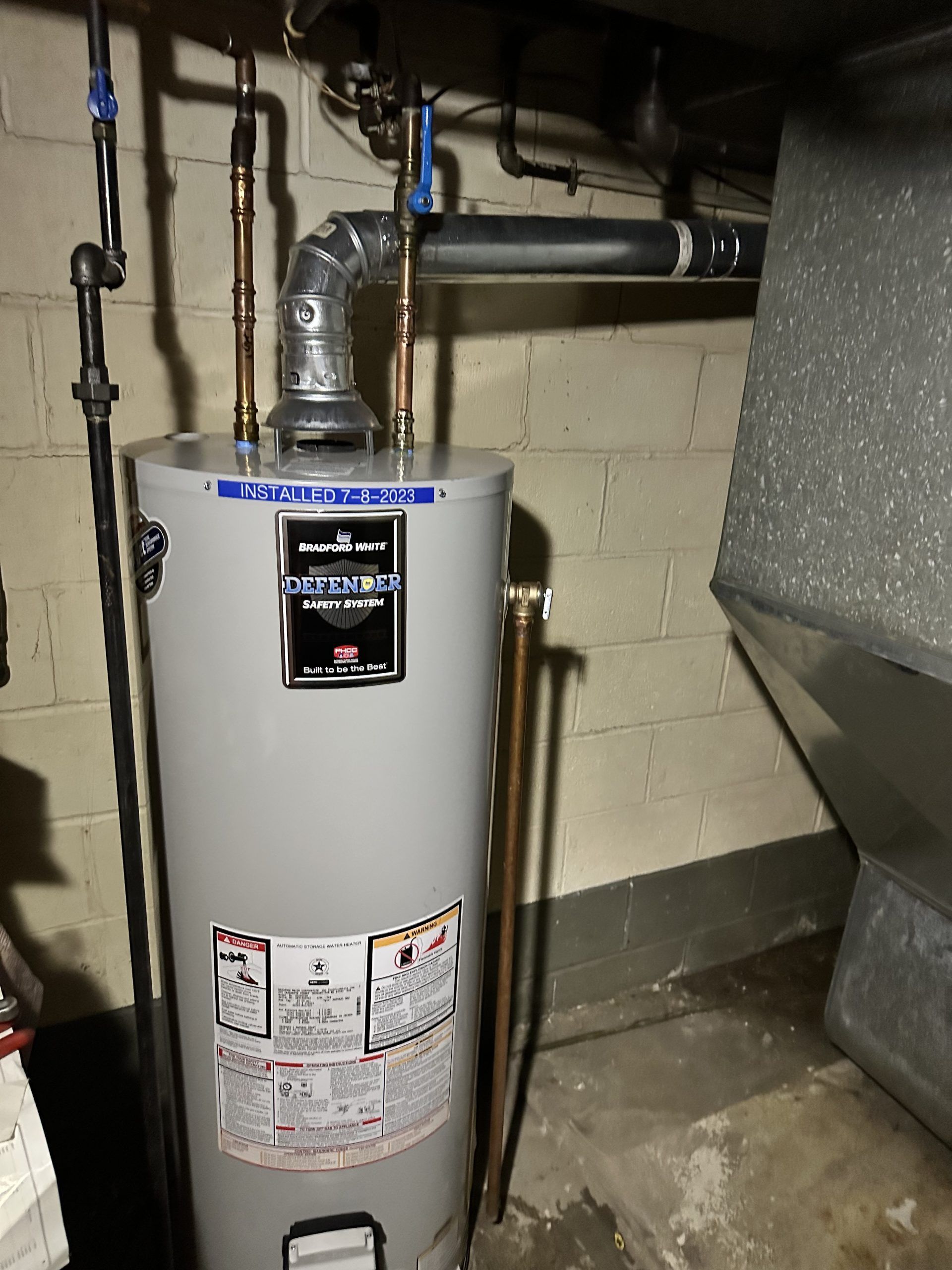 Water heater in a basement, with copper pipes and a silver exhaust pipe.
