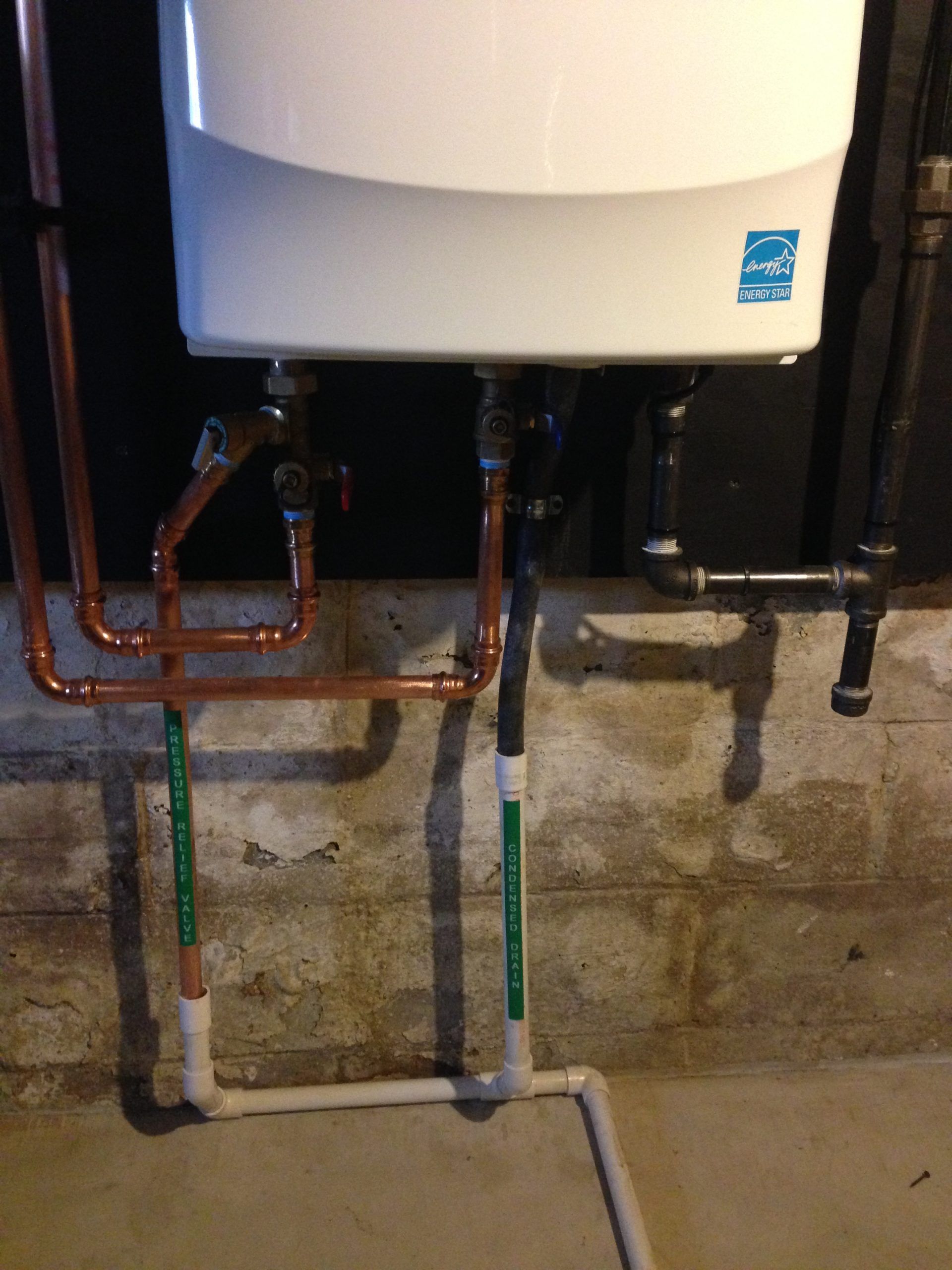 Water heater with copper and plastic pipes in a basement.