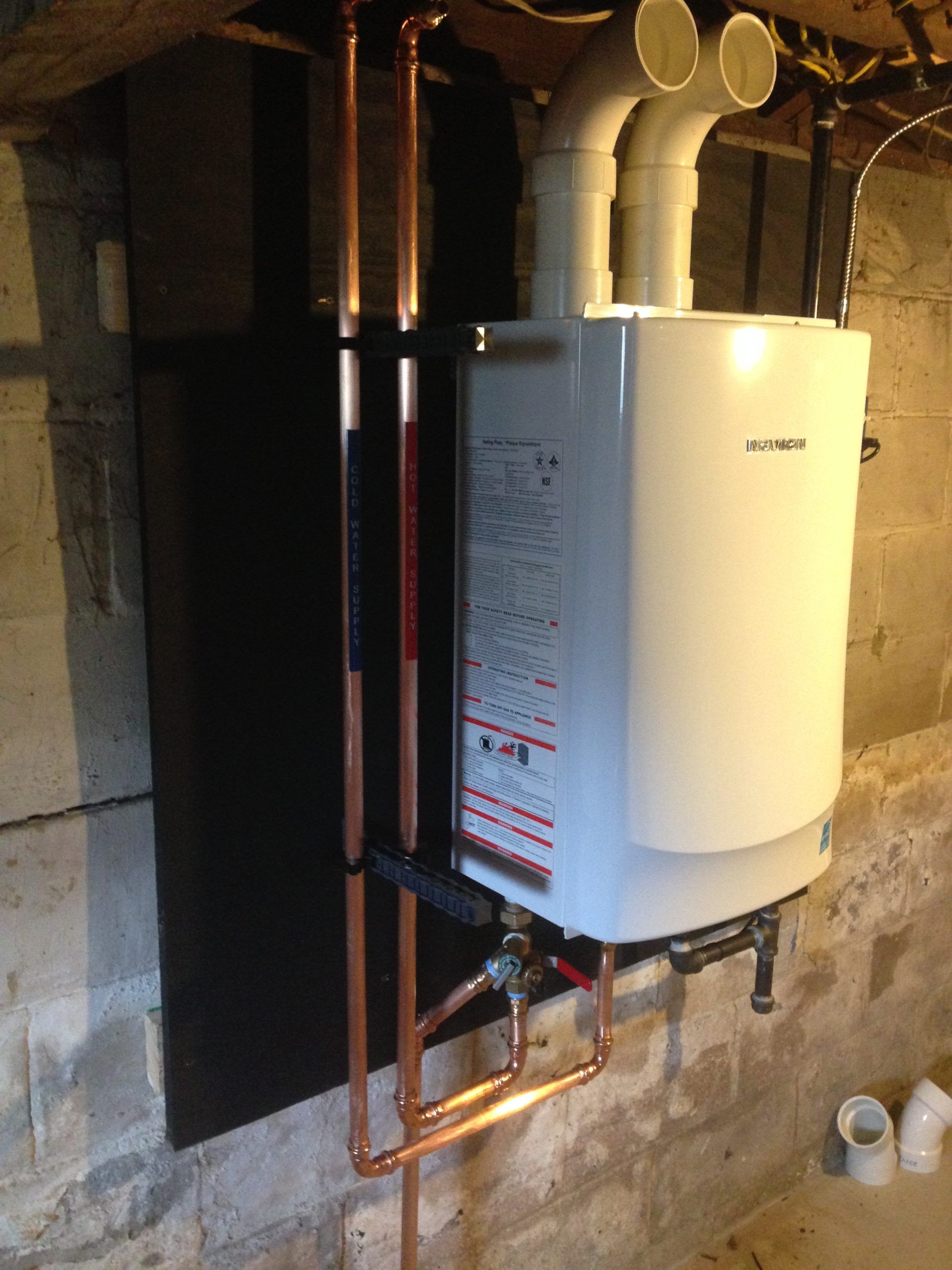 White tankless water heater with copper pipes in a basement.