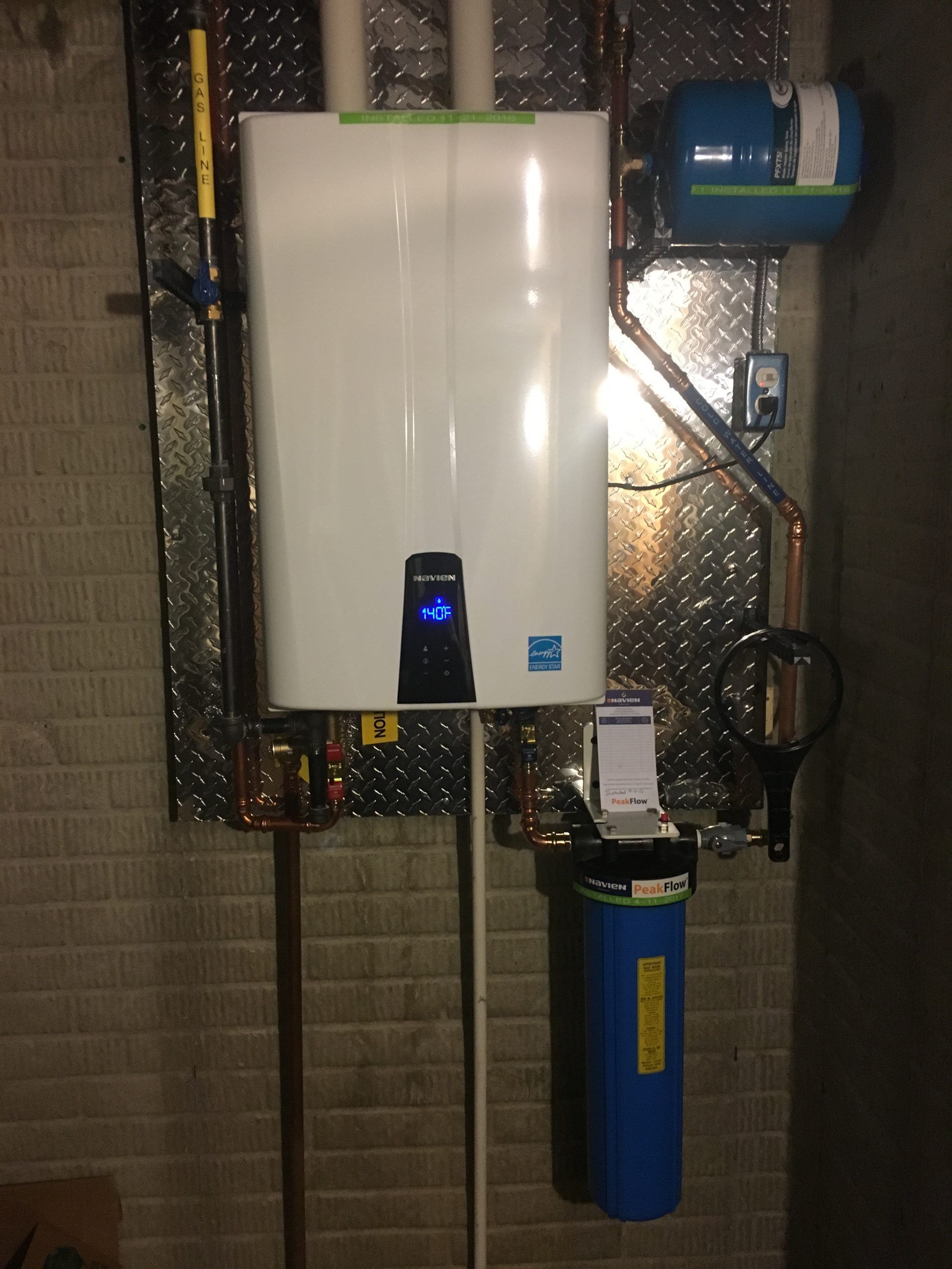 White tankless water heater, water filter, and expansion tank mounted on a basement wall.