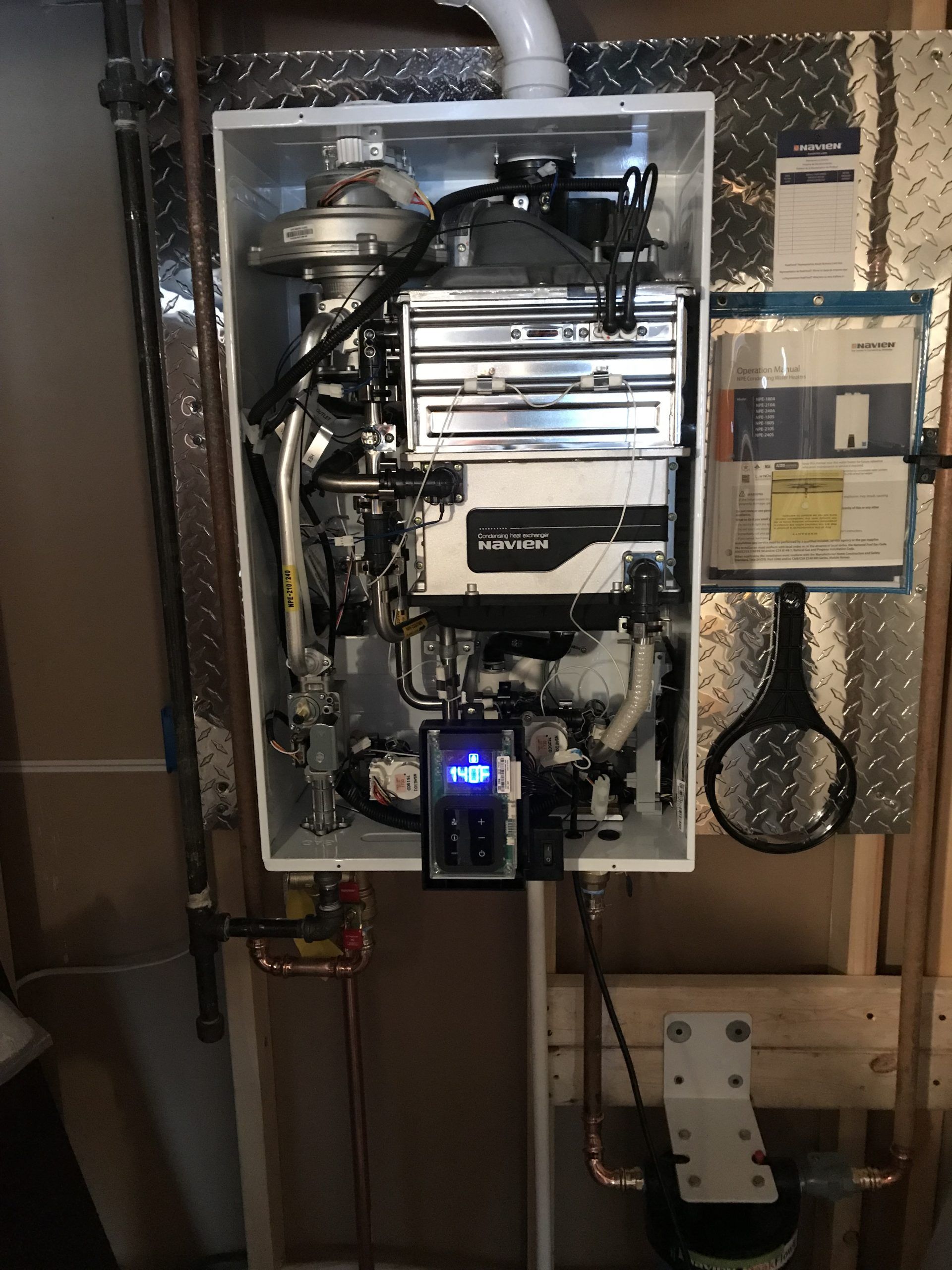 Wall-mounted gas-fired water heater with digital display, pipes, and metal surfaces, installed in a utility space.