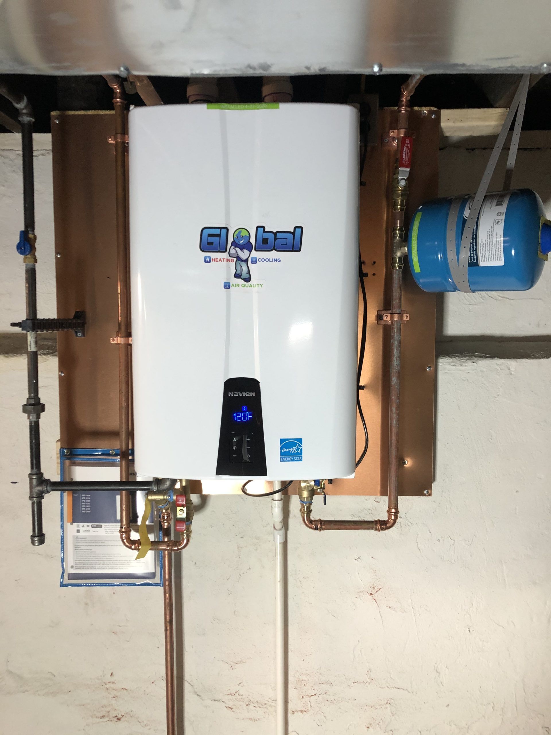 White tankless water heater with copper pipes, blue expansion tank, and wall-mounted in a basement.