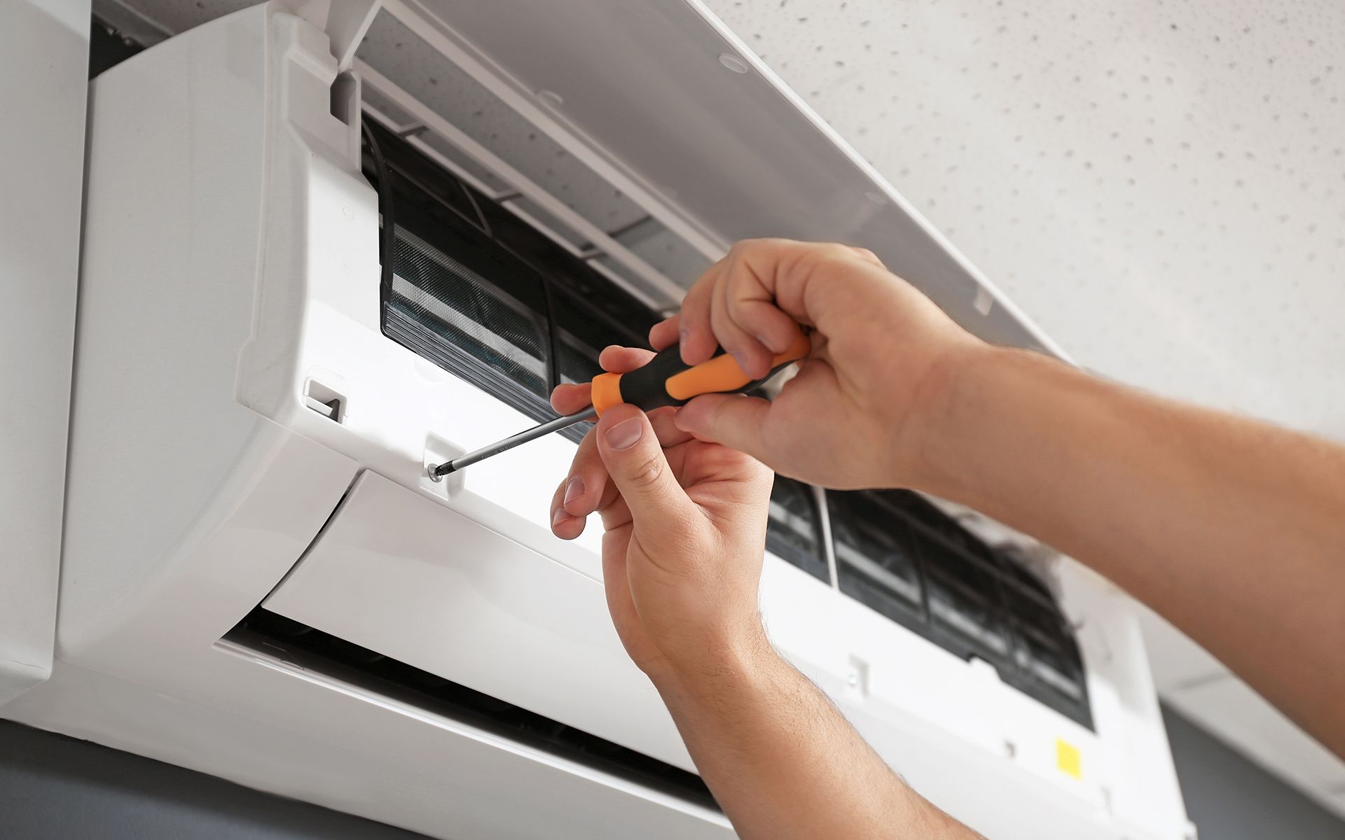 Person using a screwdriver to repair a white air conditioning unit on a ceiling.