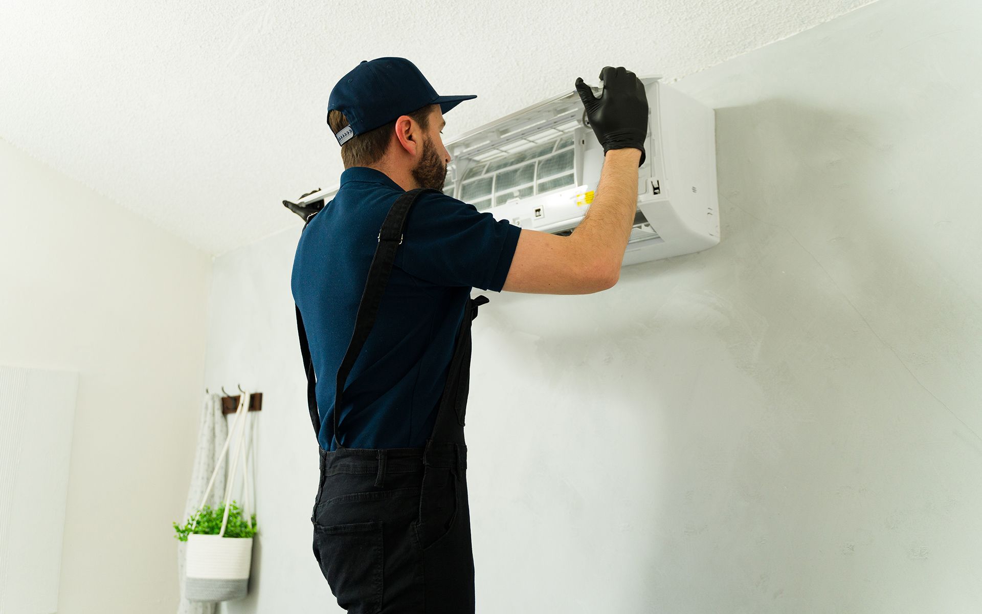 Man in uniform installing wall-mounted air conditioner unit. White wall background.