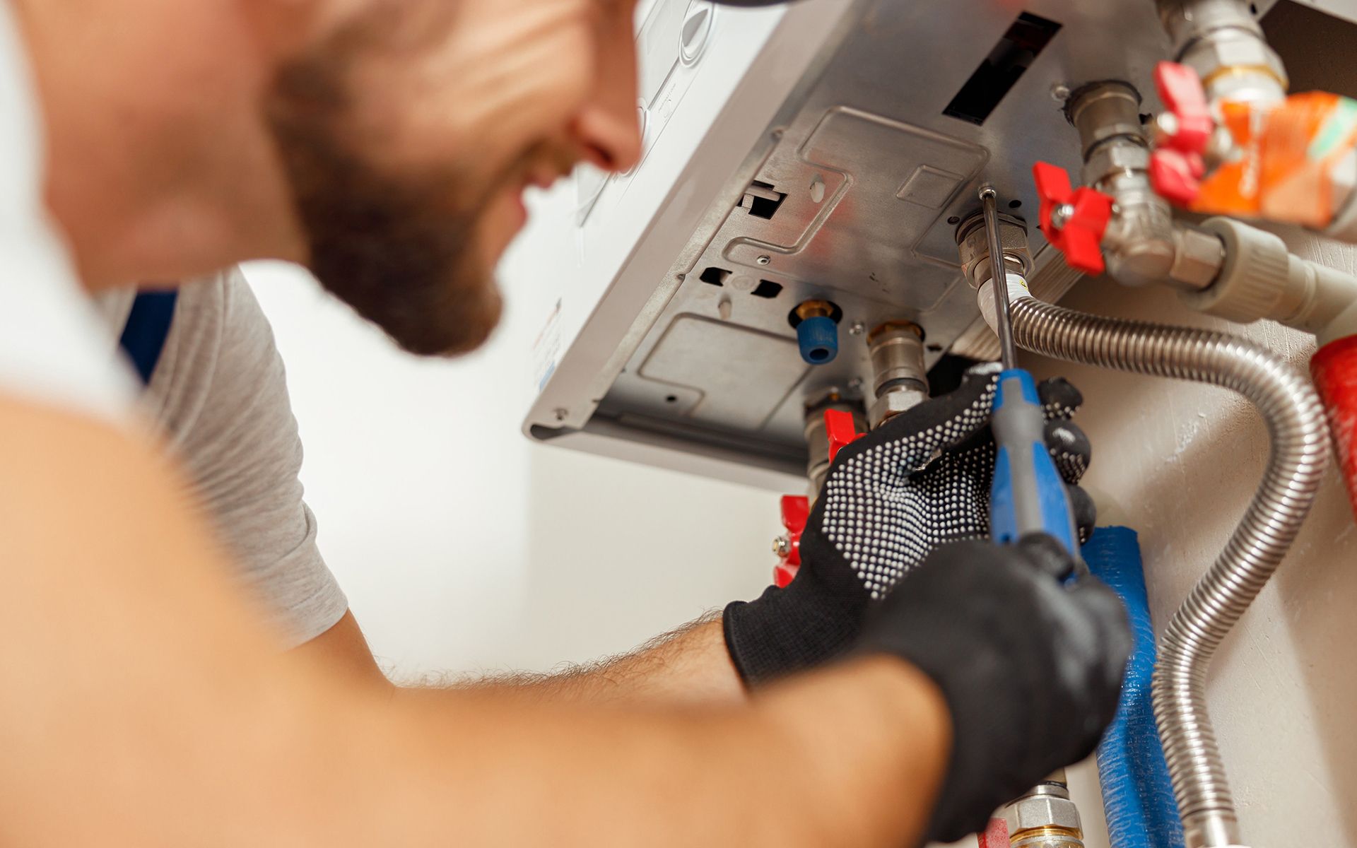 A person in black gloves using pliers on a boiler's pipes, indoors.