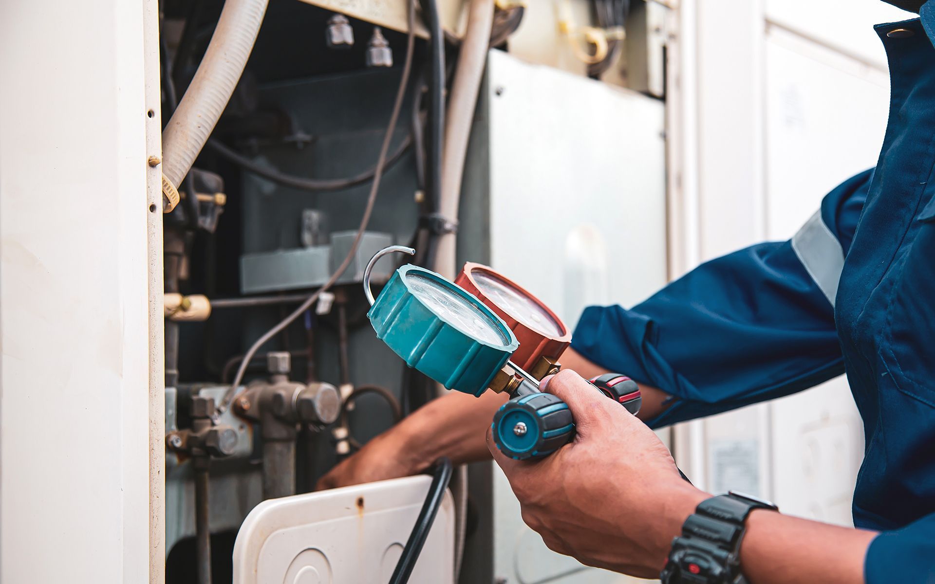 HVAC technician in blue overalls checks gauges on machinery outdoors.