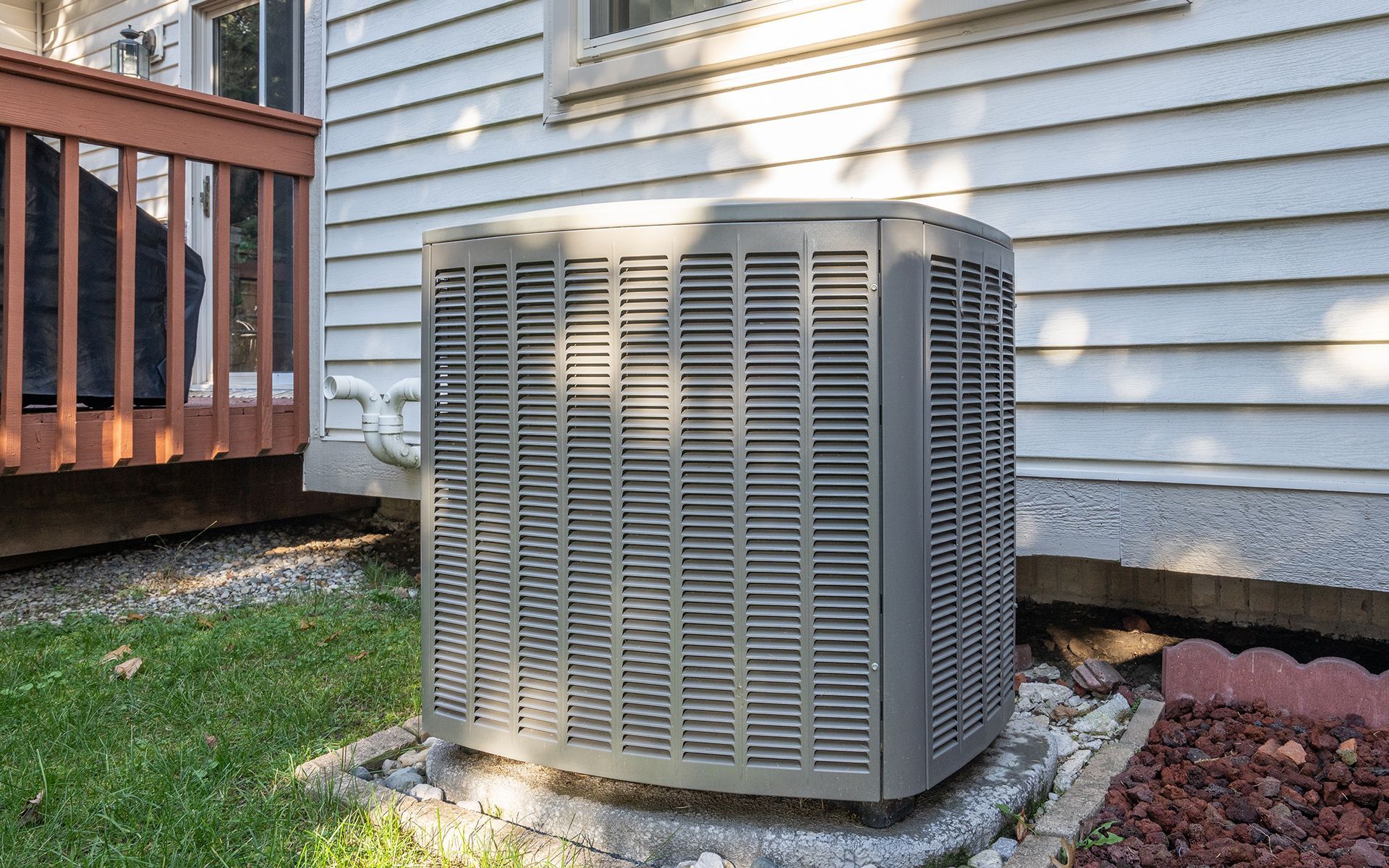 Air conditioning unit outside a white house on a concrete slab.