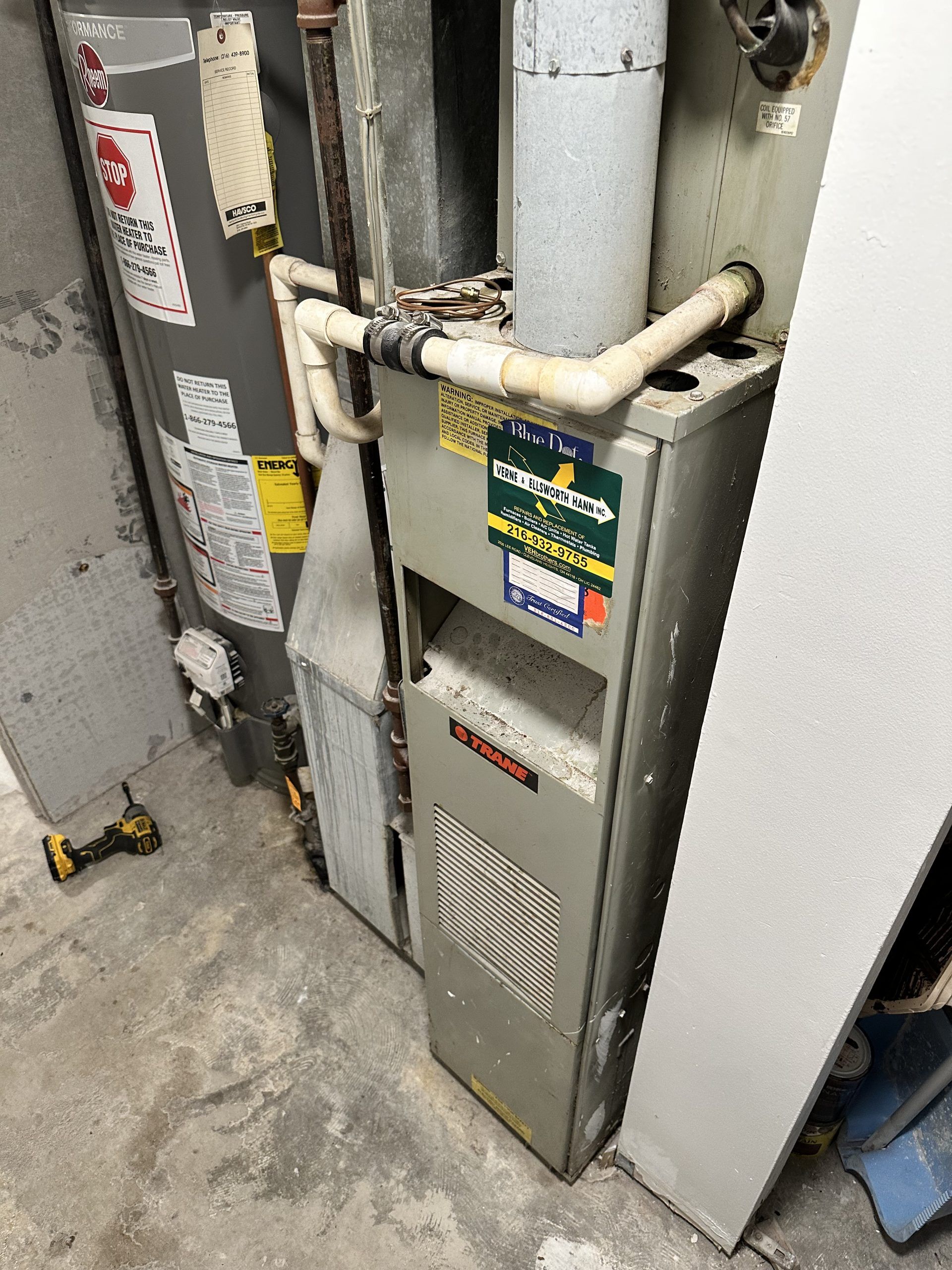 Furnace and water heater in a basement. Metal units, pipes, and a concrete floor.