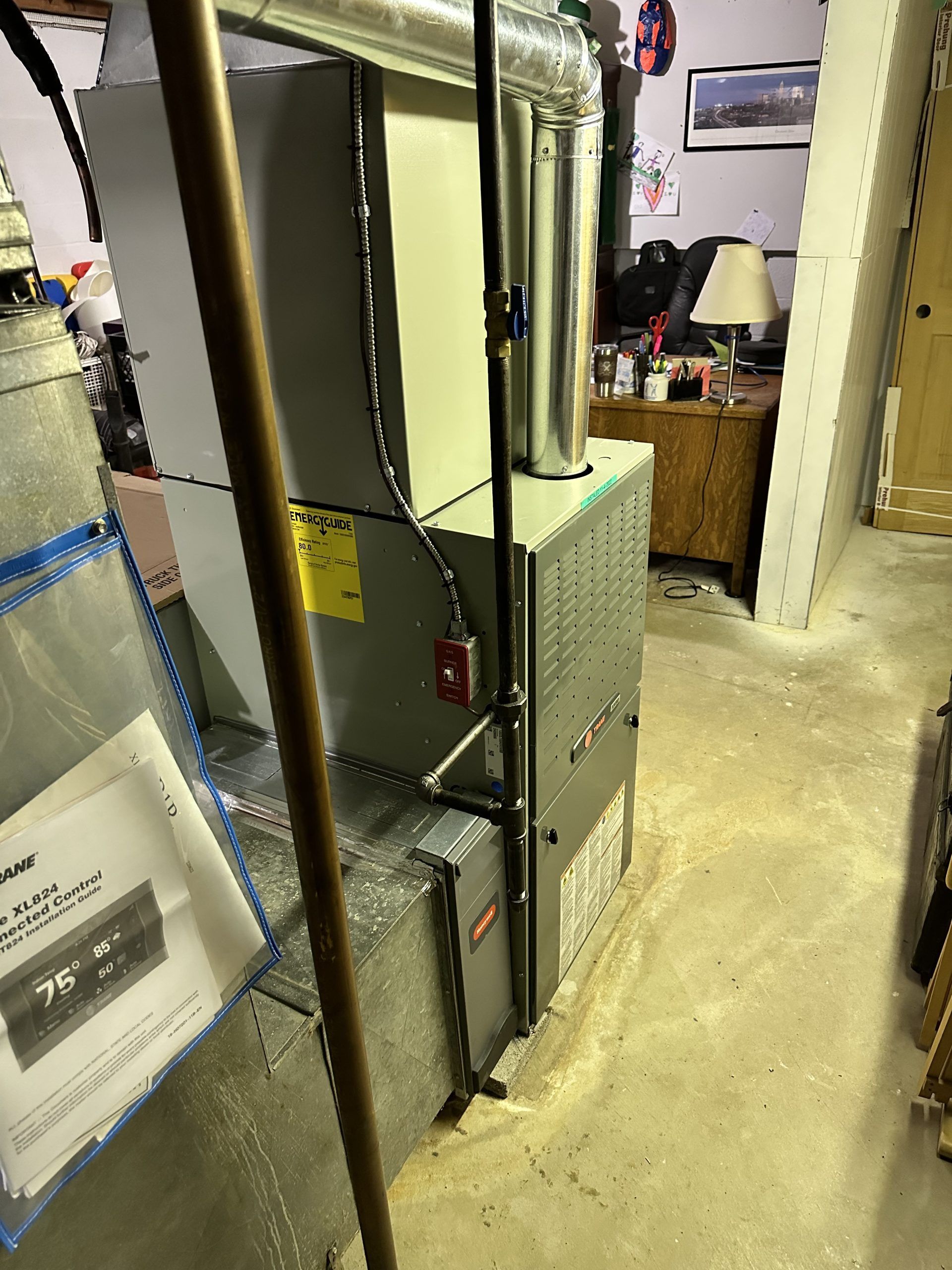 Furnace in a basement. Silver metal unit with vent pipe, electrical lines, and a fire alarm.