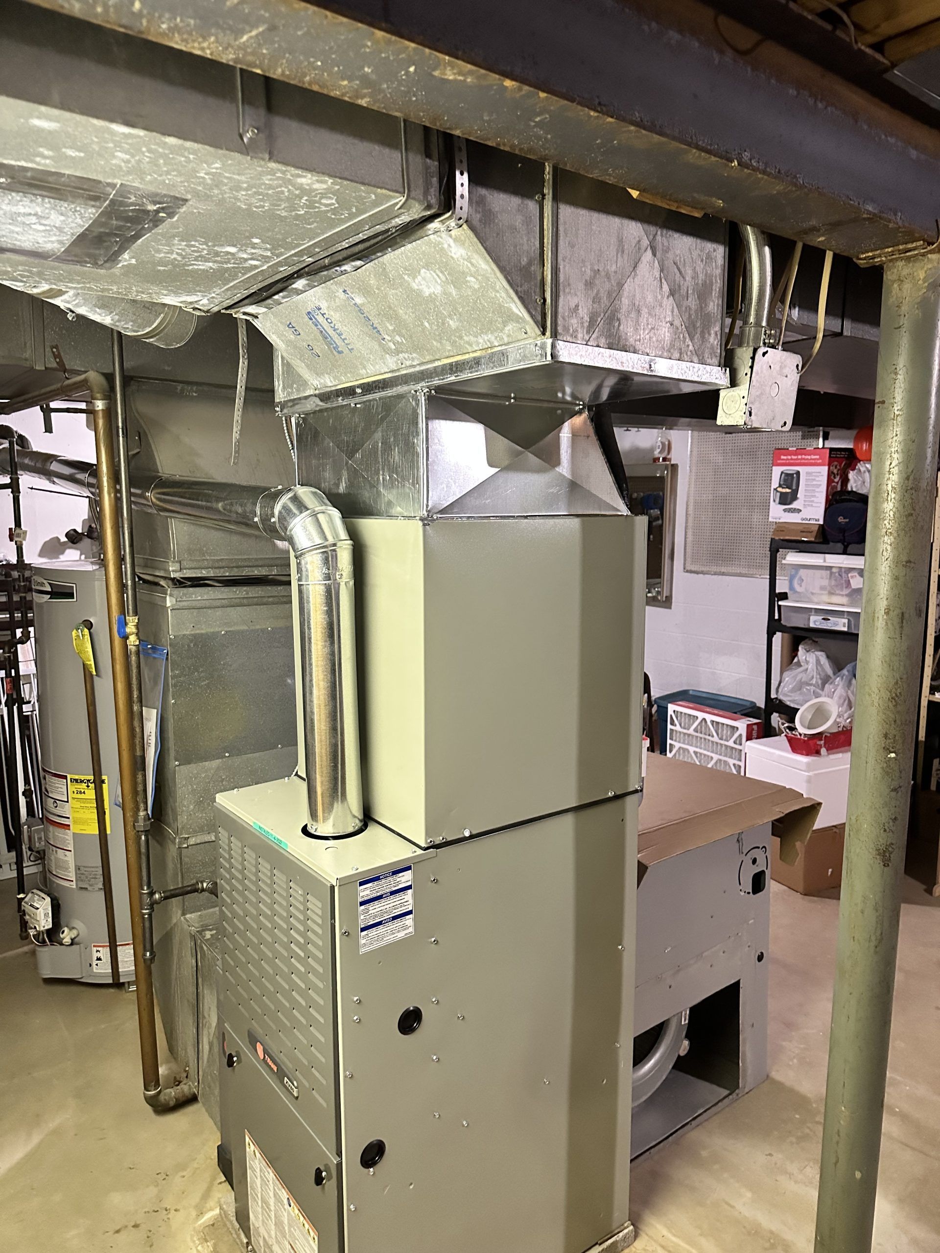 A furnace and ductwork system in a basement setting. The equipment is gray and silver.