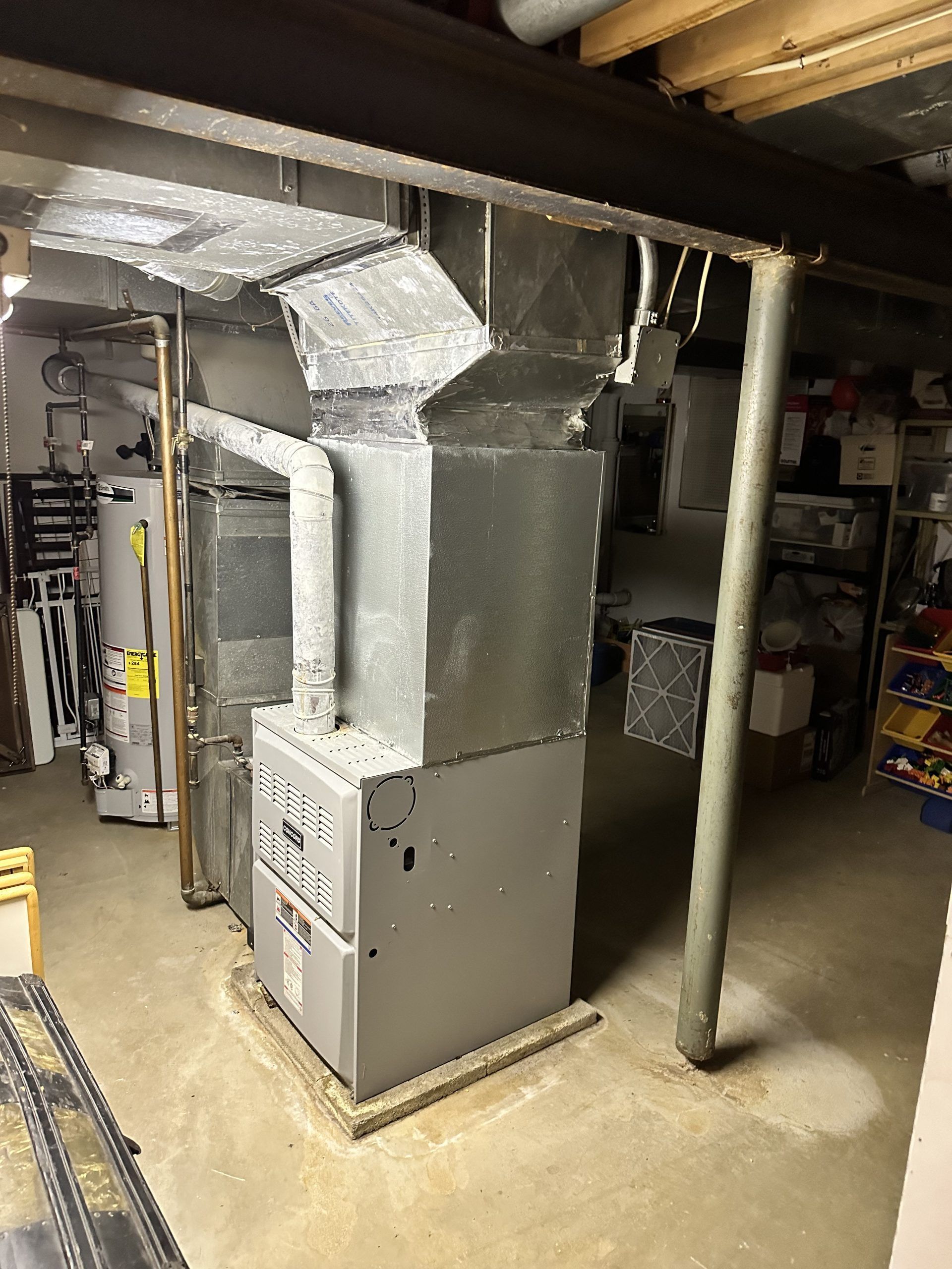 Furnace and ductwork in a basement. Metal components and pipes against concrete and a beam.