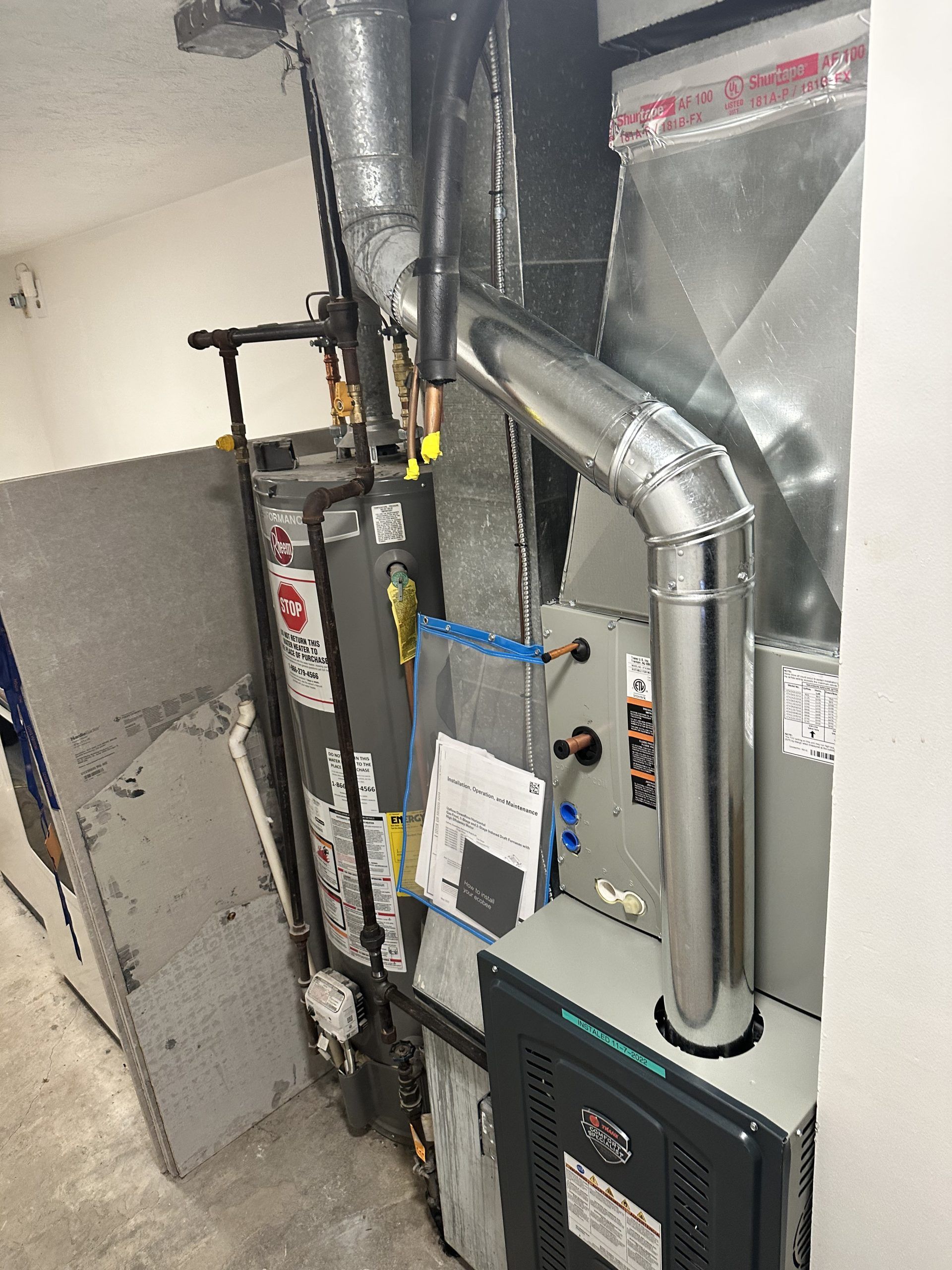 A furnace and water heater are installed in a utility closet with ductwork and plumbing.