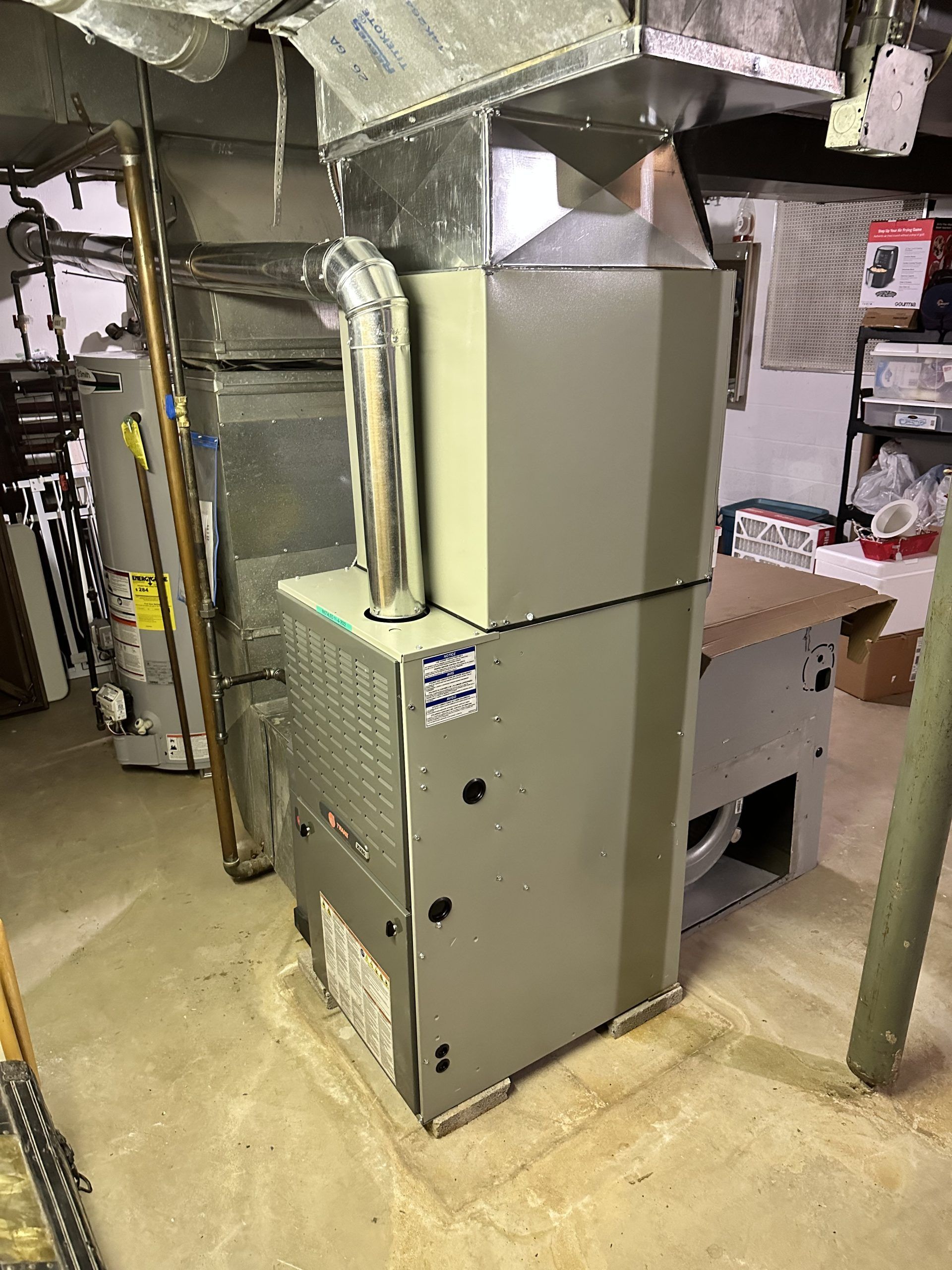 Furnace unit in a basement. It's gray with attached ductwork. A water heater is in the background.