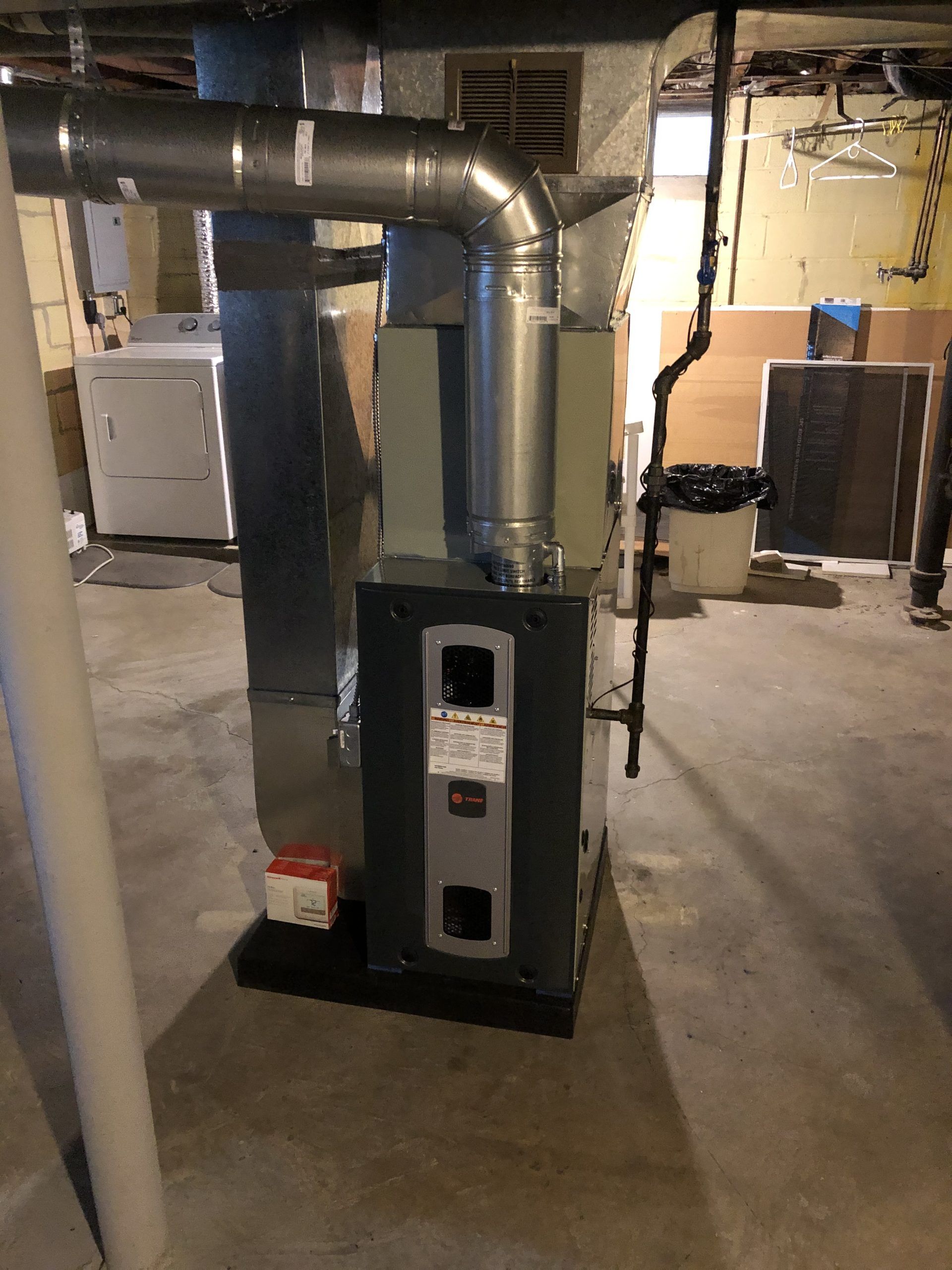 Furnace unit with ductwork in a basement setting near a laundry area. Gray and silver tones.
