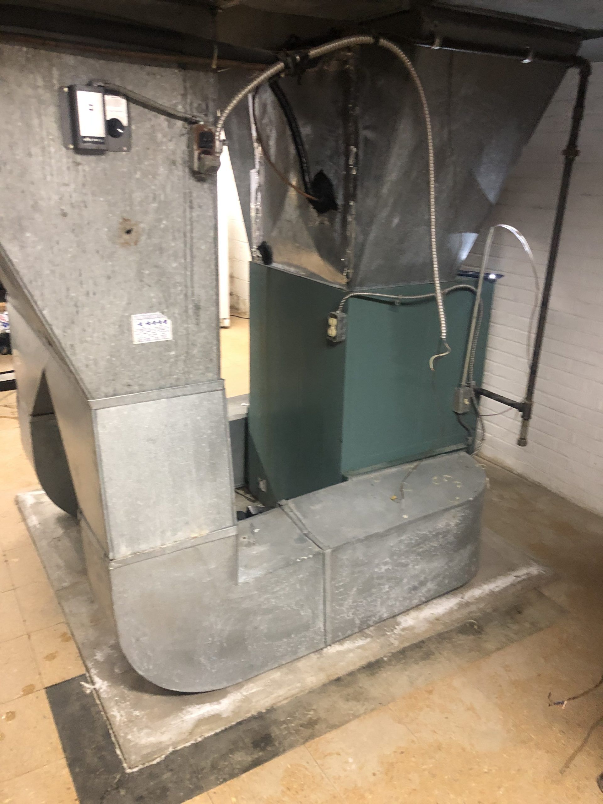 A furnace with silver ductwork and a green body in a concrete-floored basement.