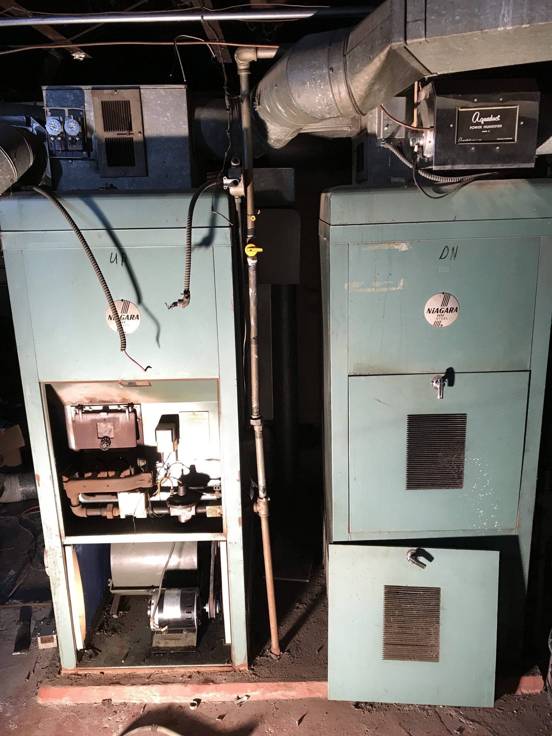Two vintage, light blue heating units in a basement. One unit's door is open, revealing inner components. 