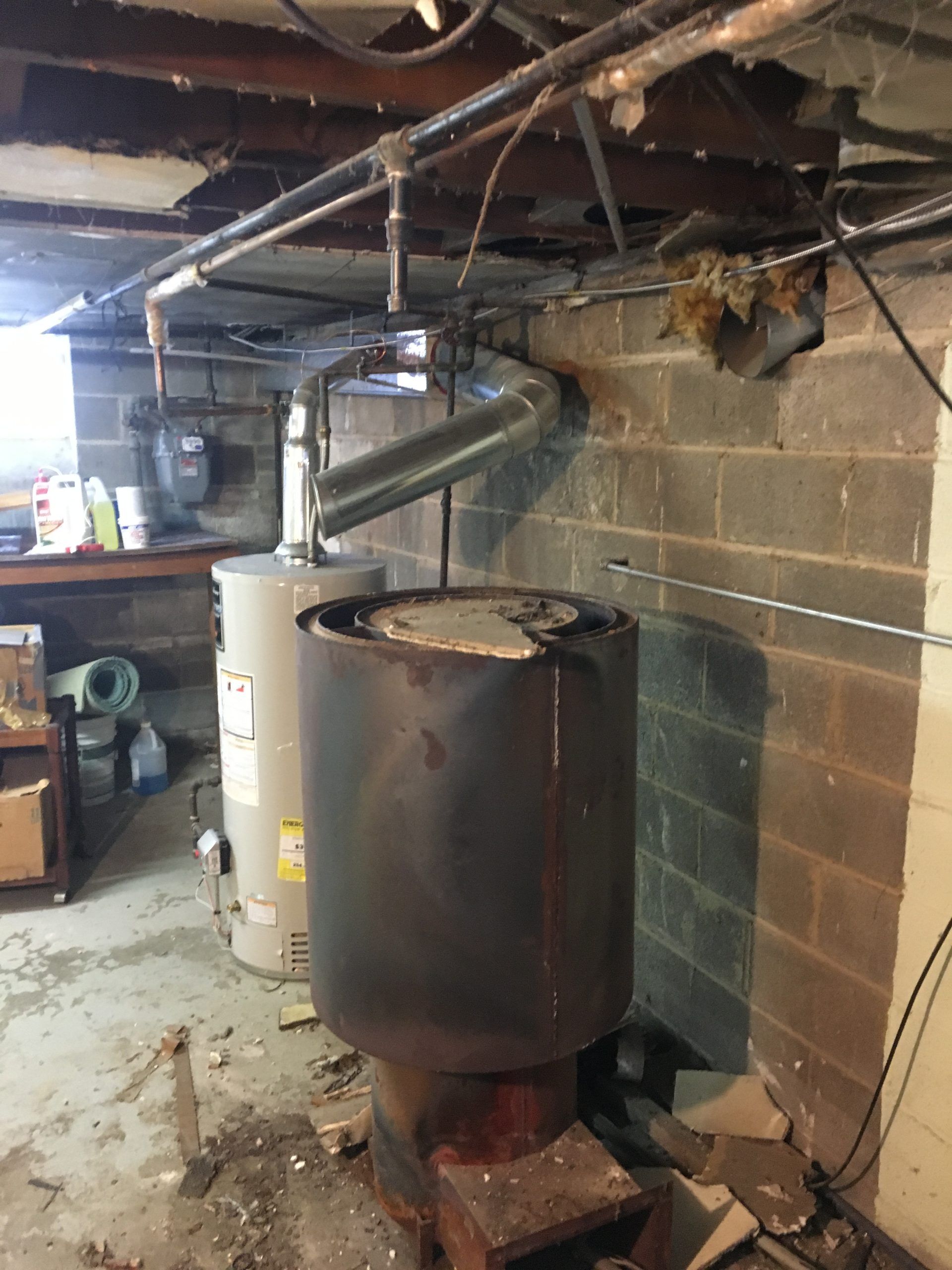 Basement with old furnace and water heater; ductwork and pipes overhead, cinderblock wall.