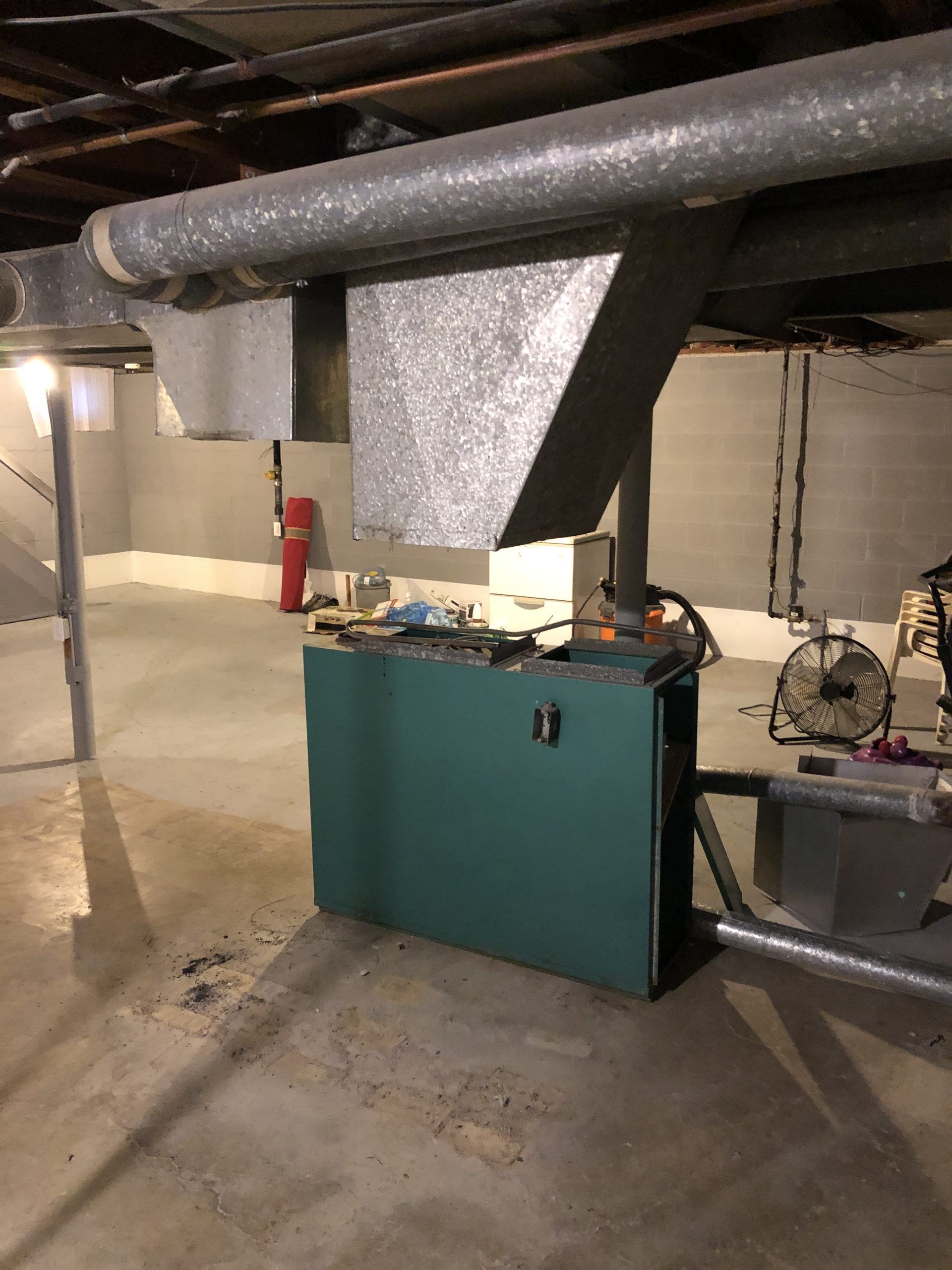 Green furnace in a basement with ductwork overhead.