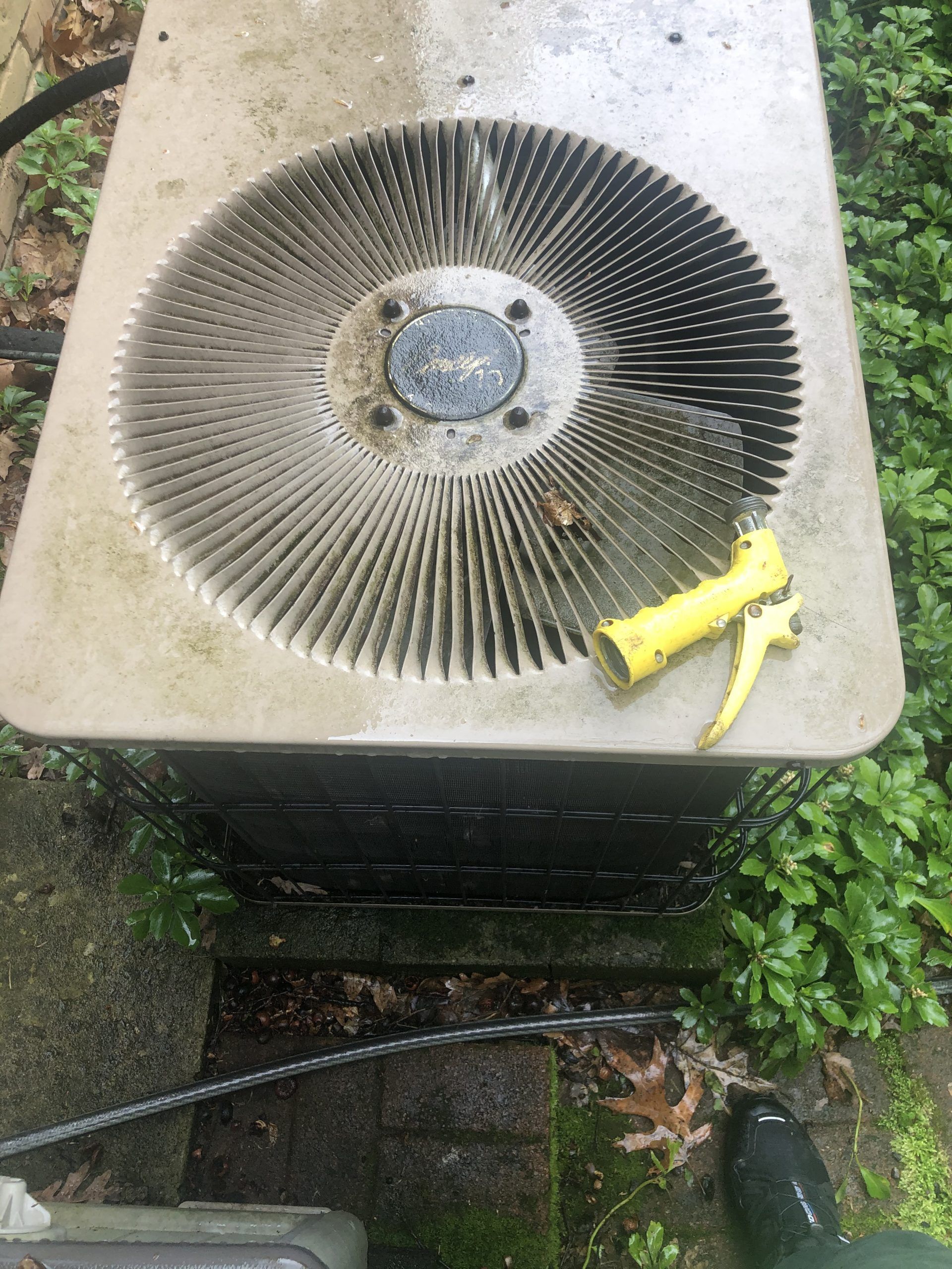 A person cleaning an outdoor air conditioning unit with a yellow spray nozzle.