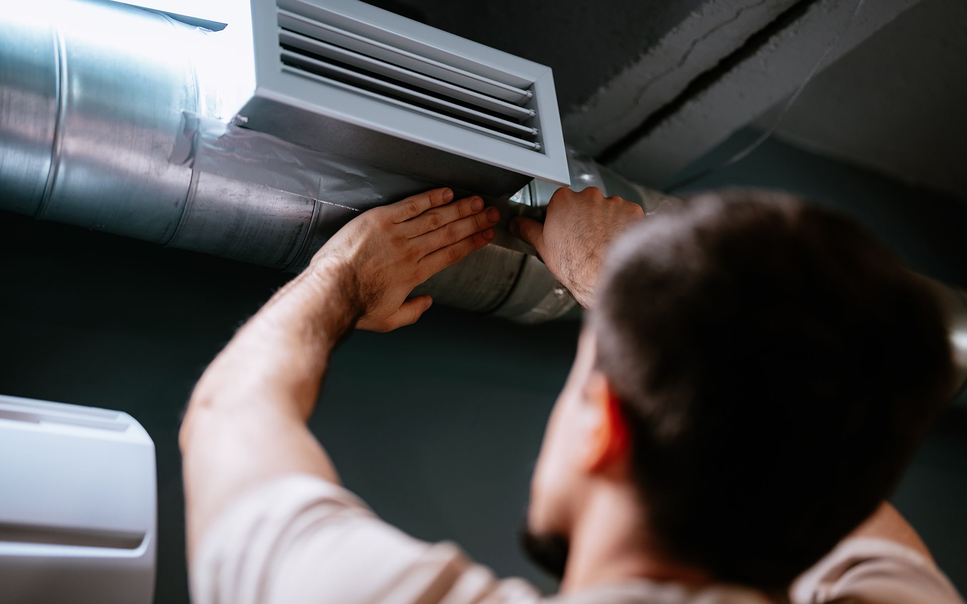 Person adjusting ductwork in a building. They are wearing a dark shirt.