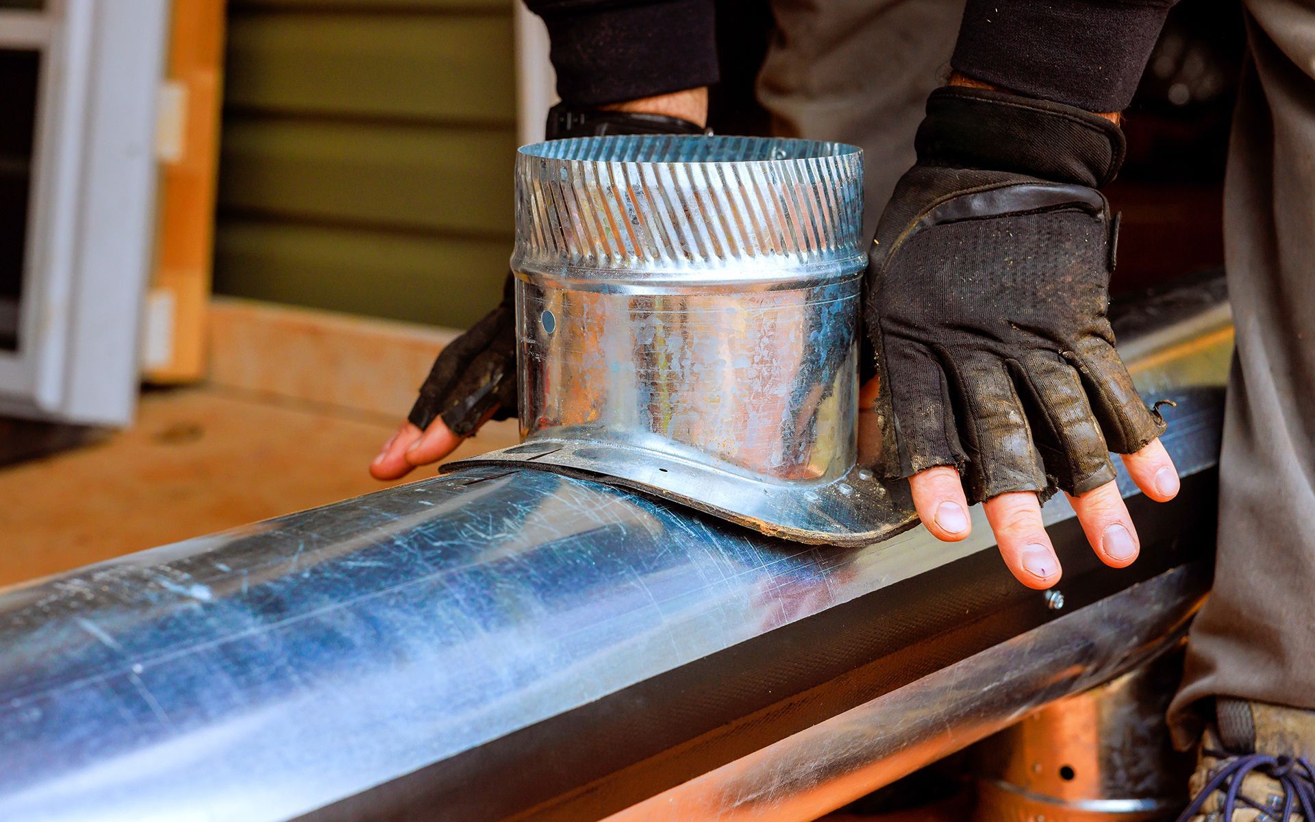 Hands in work gloves assembling metal vent pipe.