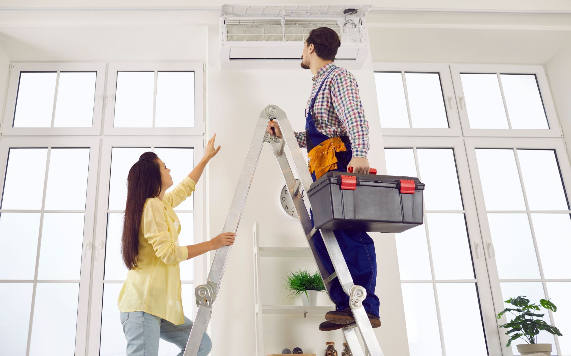Woman celebrates under an air conditioner in an office, arms raised, thumbs up.