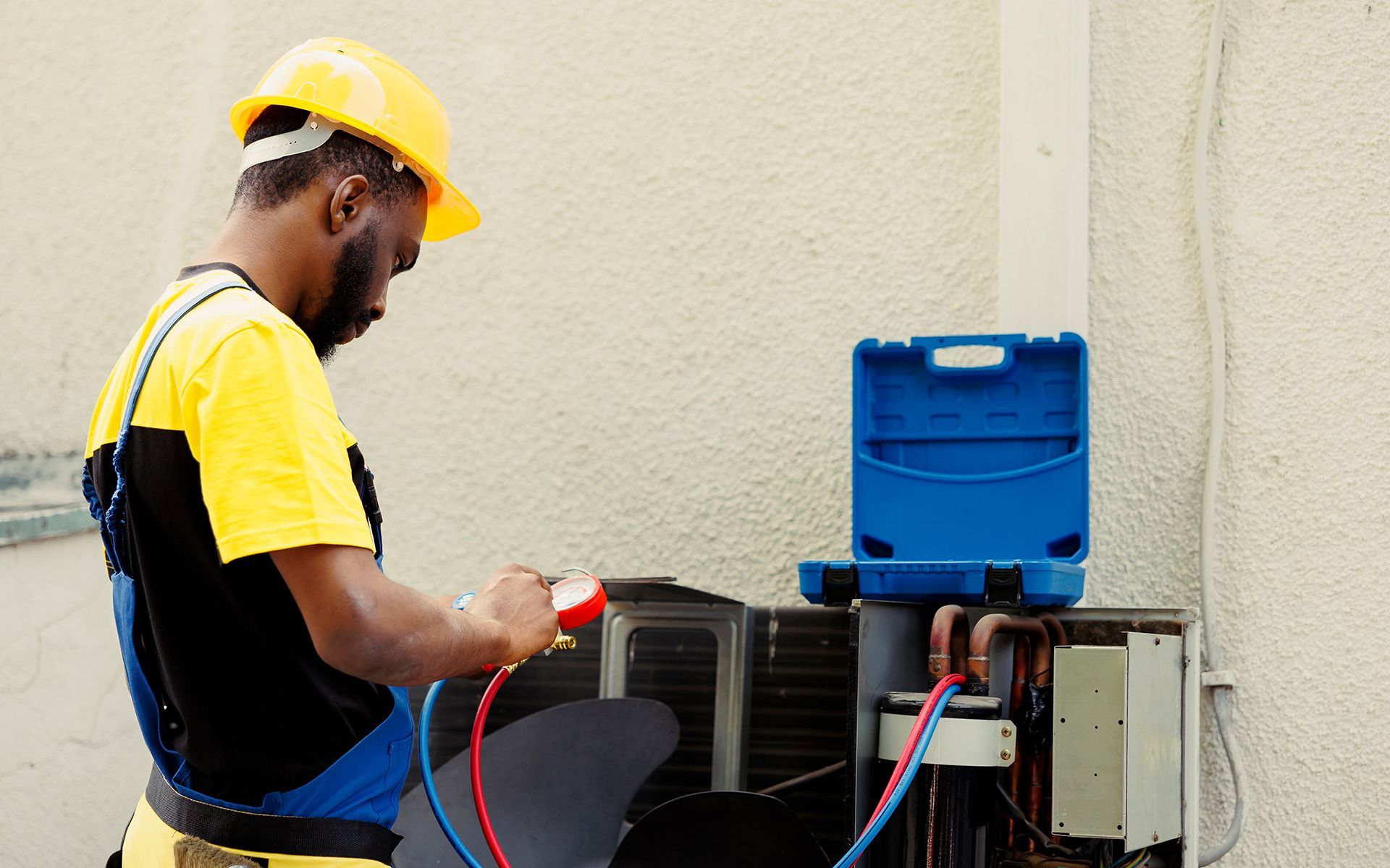 HVAC technician in yellow hard hat checks air conditioner unit.