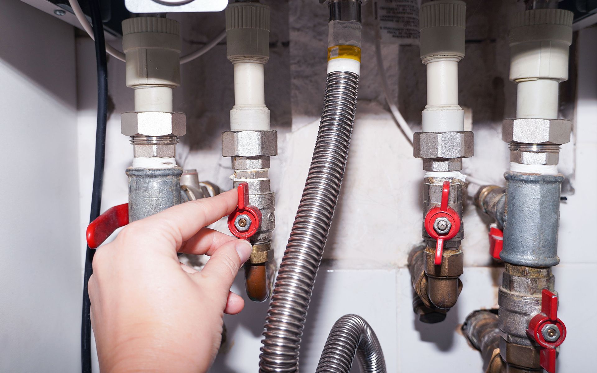 Hand turning a red valve on a water heater, close-up view.