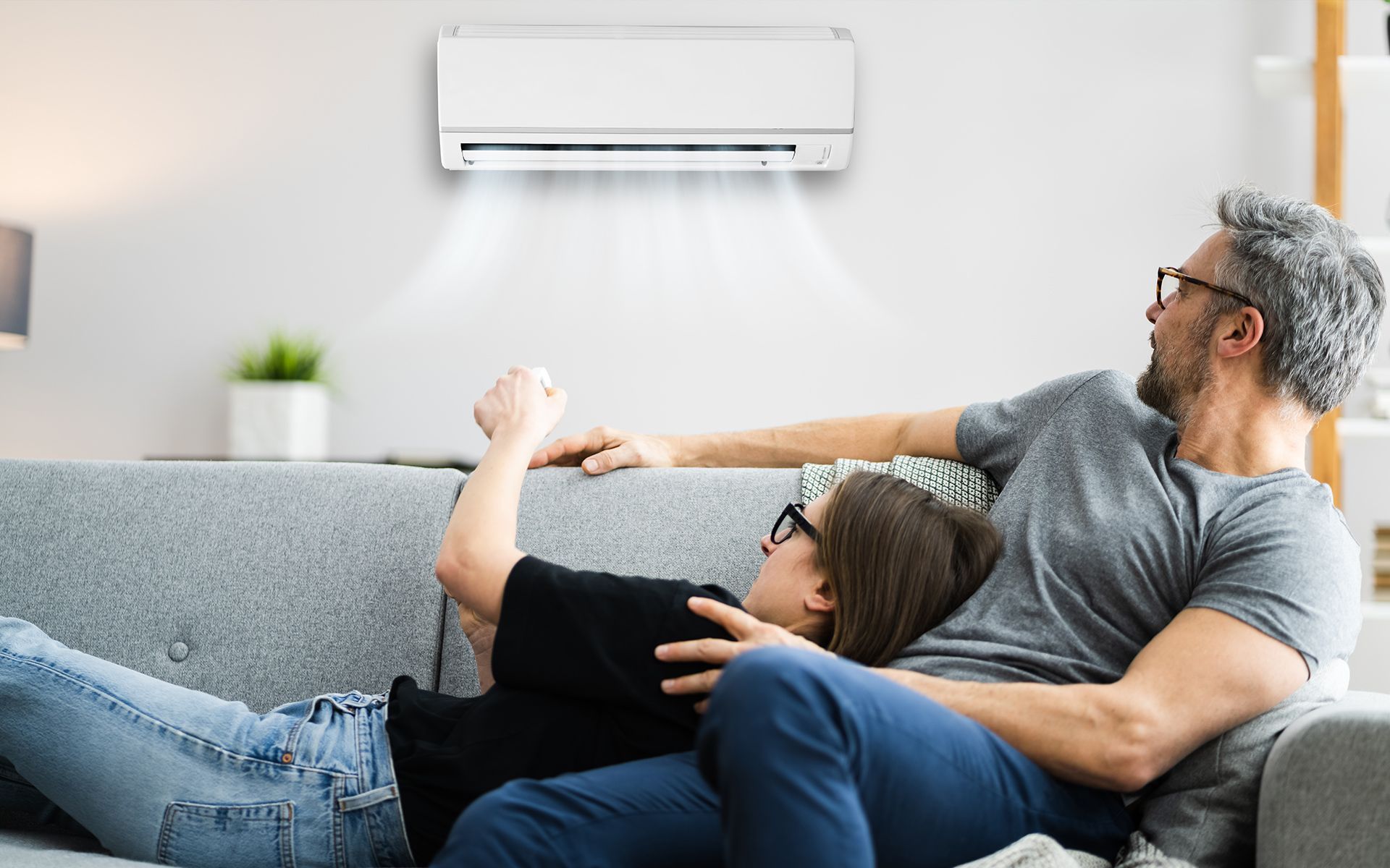 Couple relaxing on a sofa under an air conditioner blowing air.