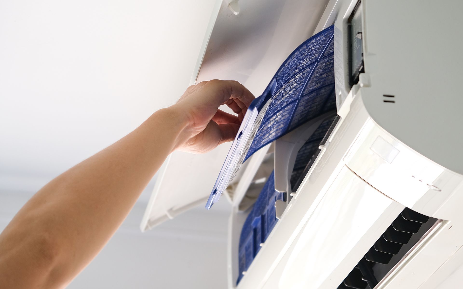 A hand removing a blue air filter from a white air conditioner unit.