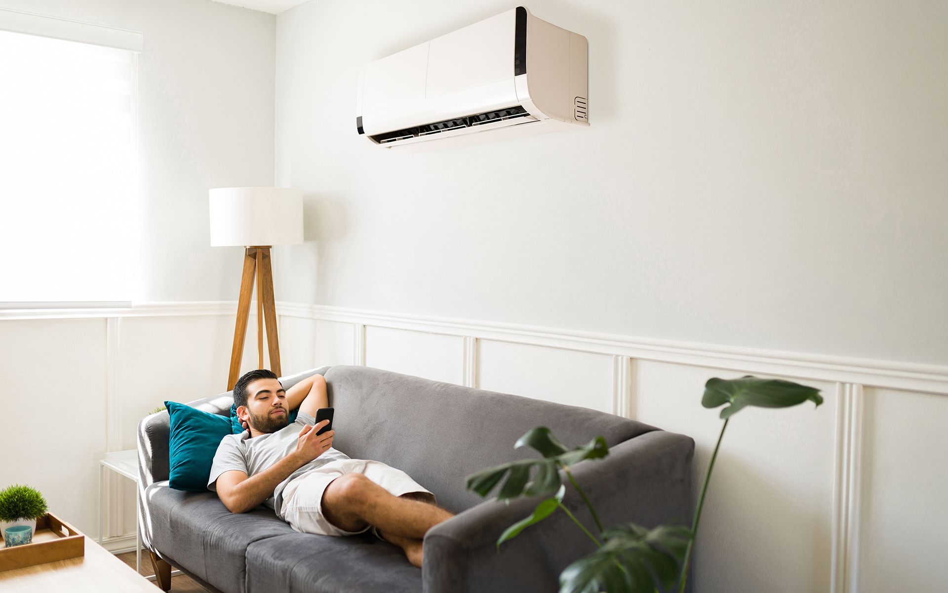 Man relaxing on a couch, using a remote. An air conditioner is mounted on the wall.