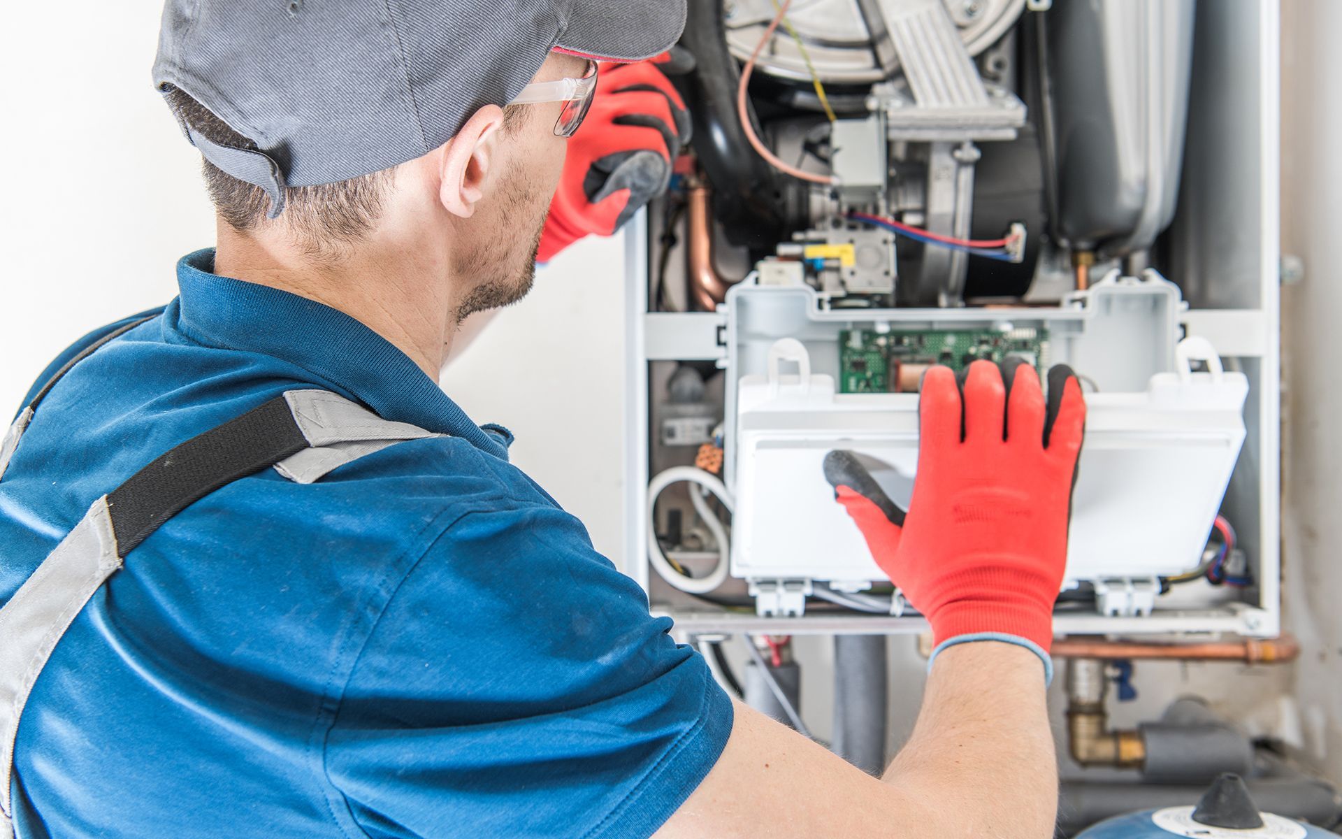 A technician in blue shirt and red gloves repairs a furnace.