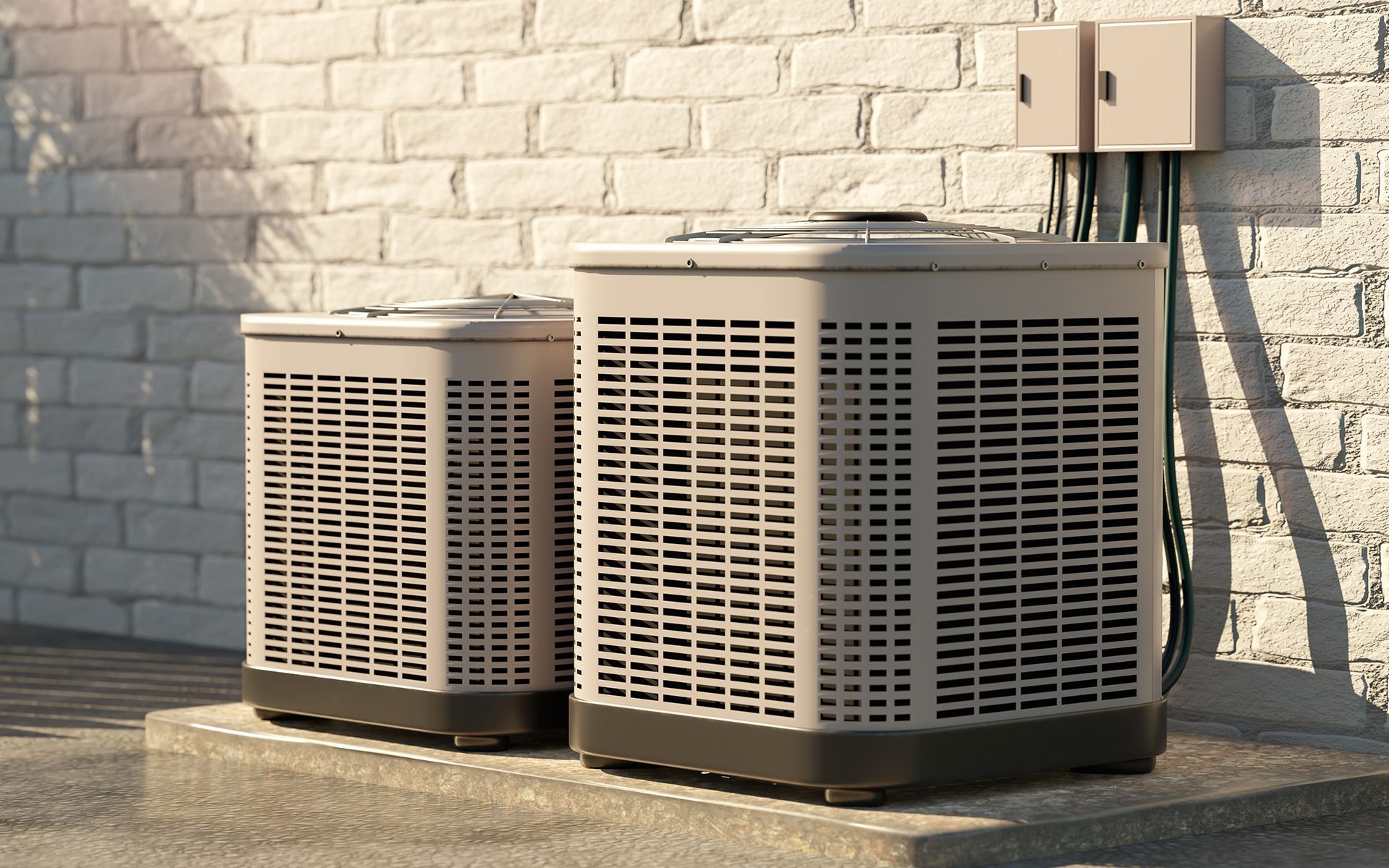 Two air conditioning units near a brick wall with electrical connections.